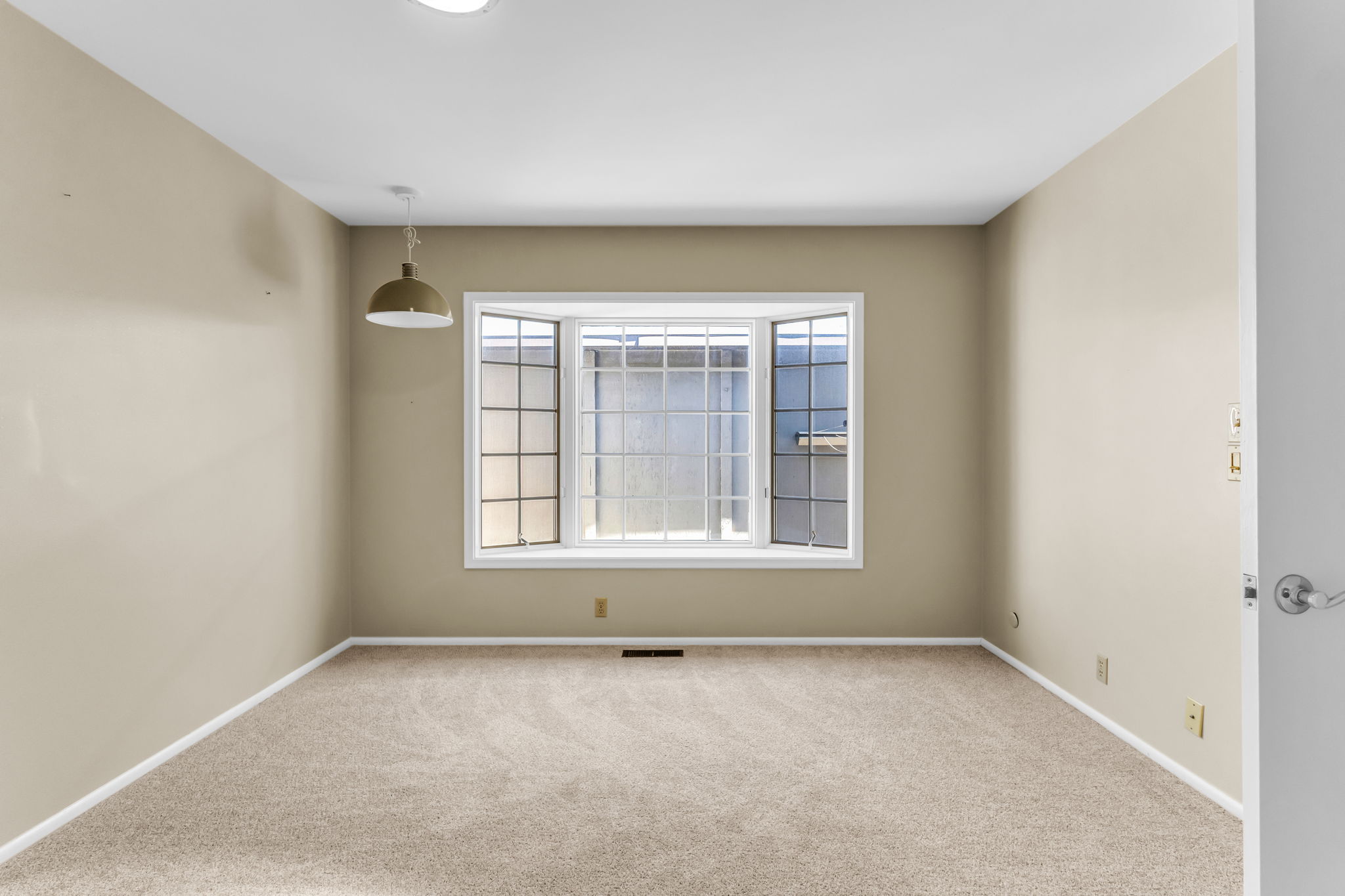 Neutral-toned interior featuring a bay window with multiple panes, recessed ceiling lighting, a suspended pendant light fixture, light-colored carpeting, and white baseboards