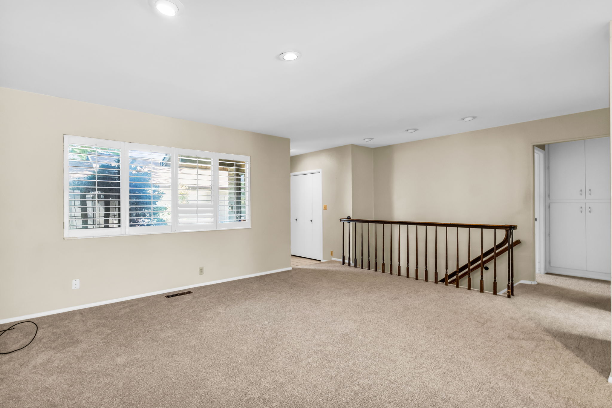 Spacious room featuring neutral carpeting, recessed lighting, and a multi-pane window with plantation shutters