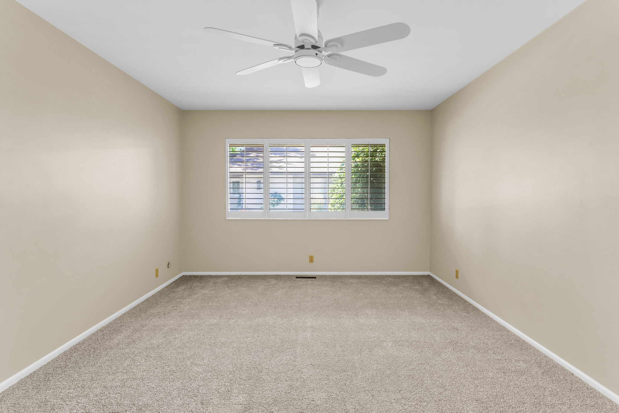 Neutral-toned room featuring a white ceiling fan, light beige walls, and carpet flooring