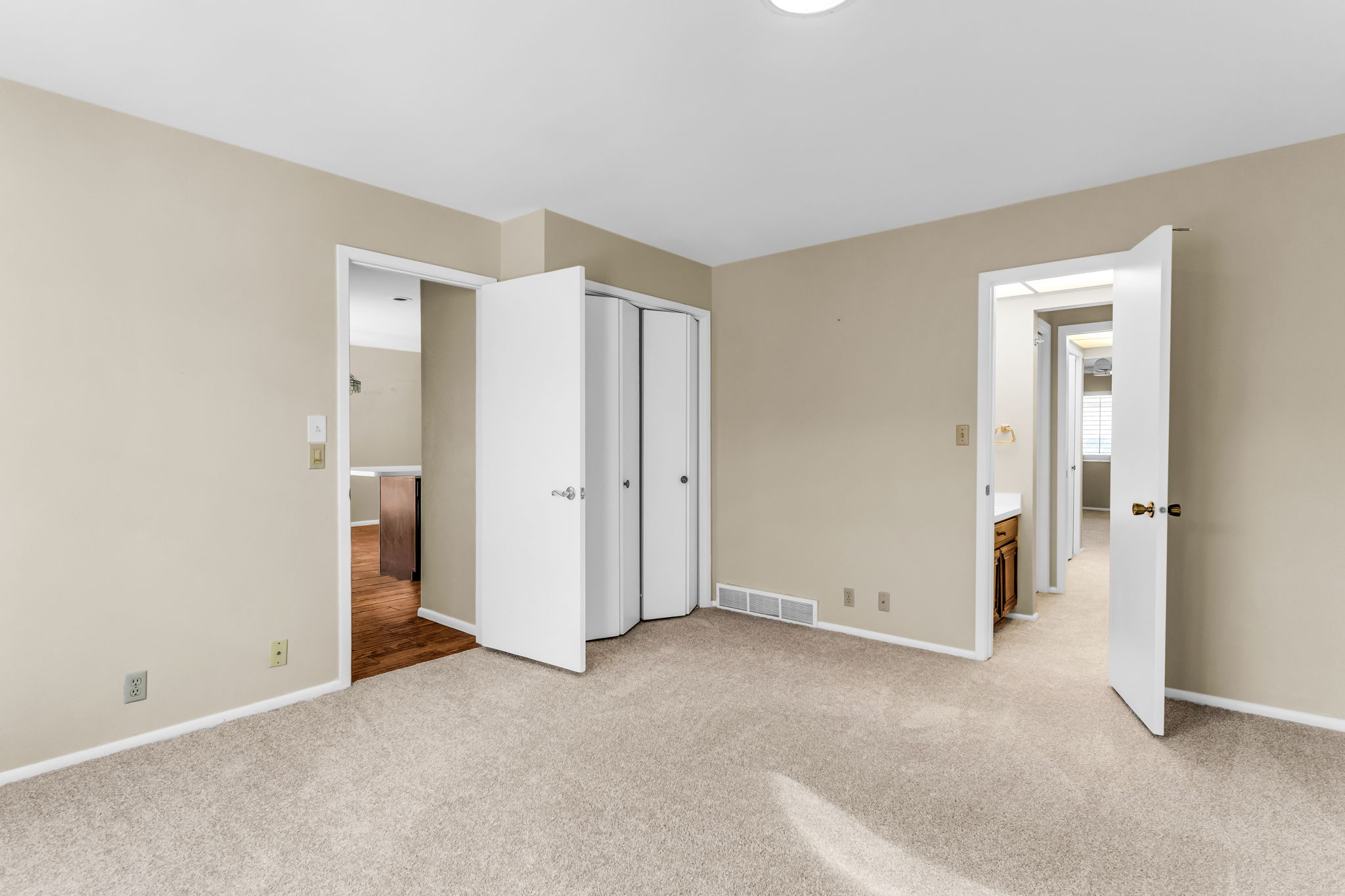 Neutral-toned carpeted room featuring a ceiling light fixture, white baseboards, and two doorways with white trim
