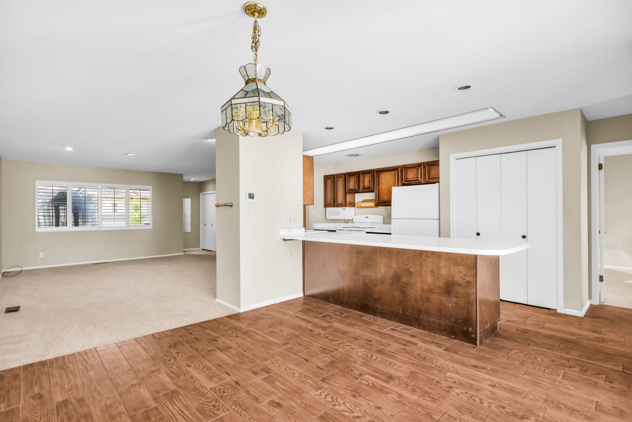 Open-concept living area featuring wood-finish flooring, a kitchen island with a white countertop, recessed lighting, and a decorative chandelier