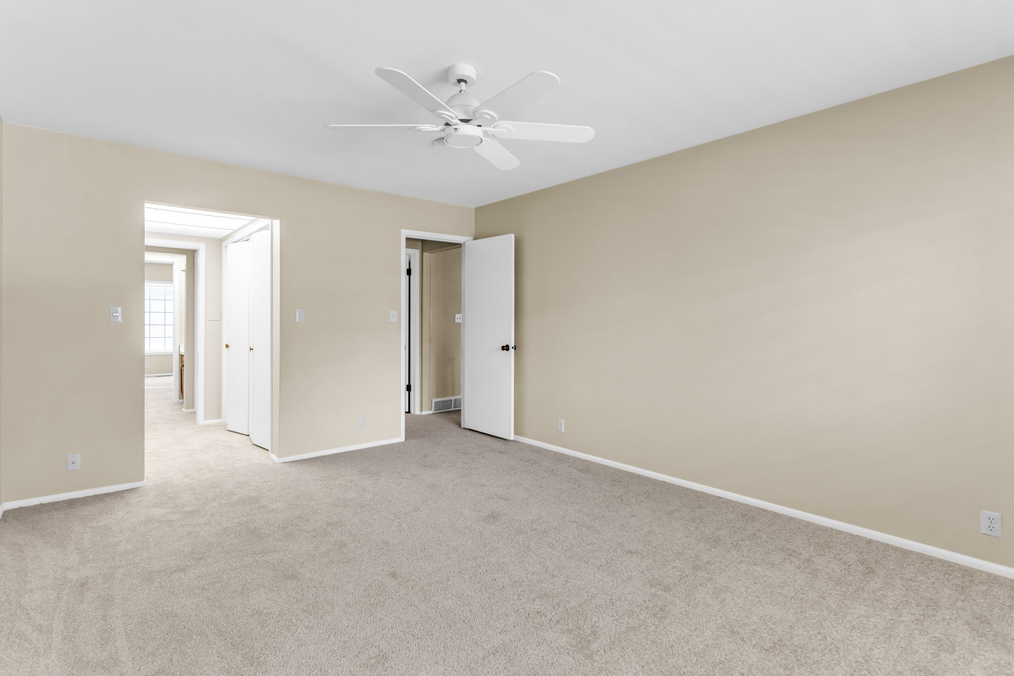 Spacious room with neutral-toned walls, light-colored carpet, and a ceiling fan