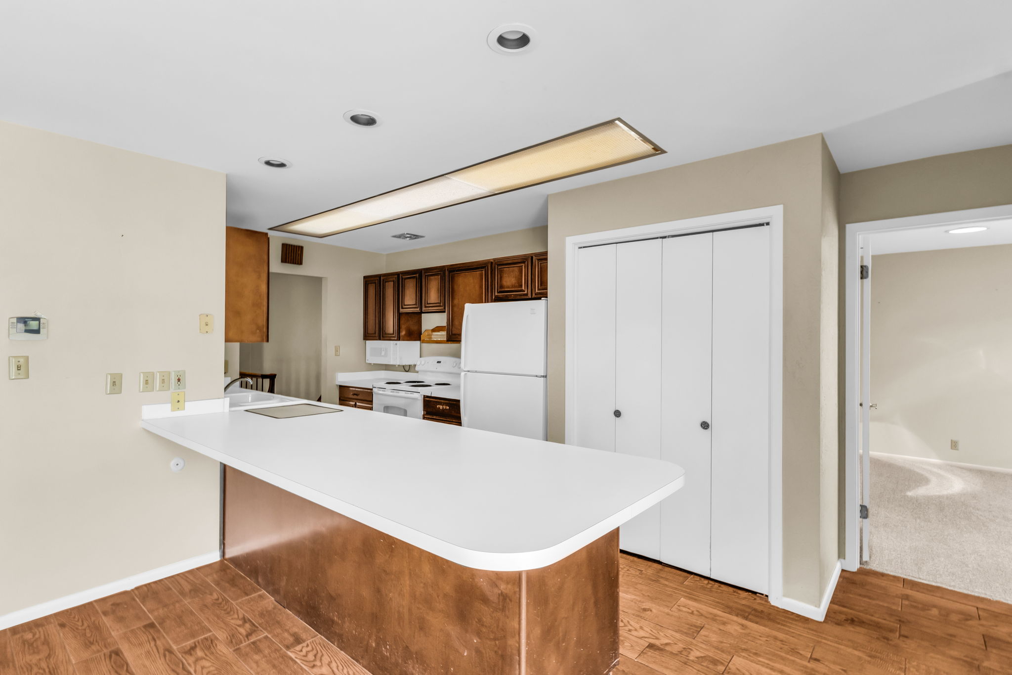 Kitchen featuring a white countertop breakfast bar, wood-finish flooring, recessed lighting, white appliances, and wood cabinetry