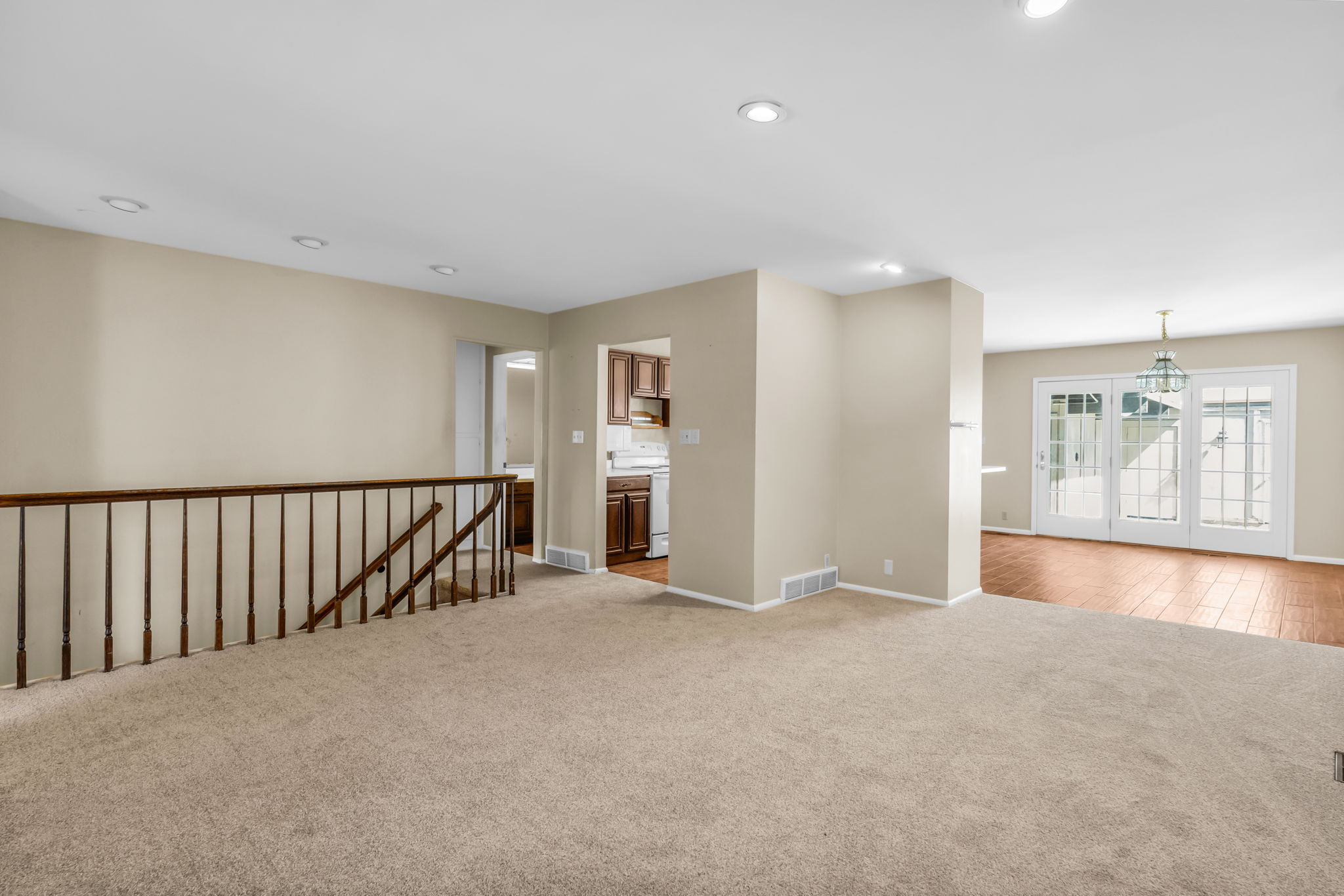 Carpeted living area featuring recessed lighting, a wood baluster railing, and neutral wall tones