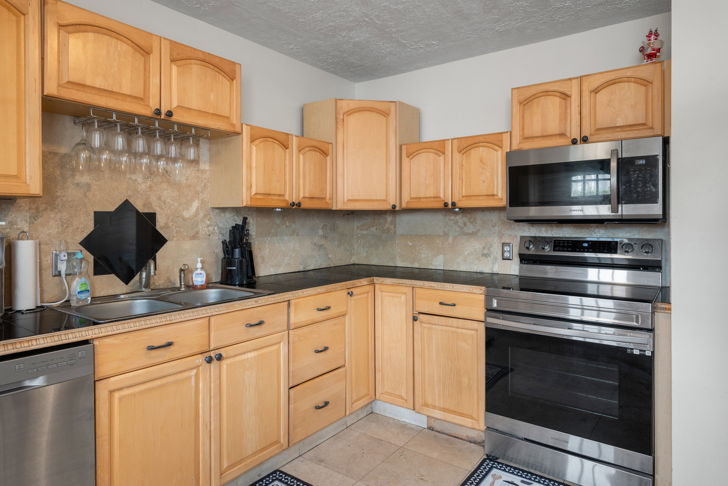 Kitchen featuring light wood cabinetry, dark countertops, a tile backsplash, and stainless steel appliances including a microwave, oven, and dishwasher