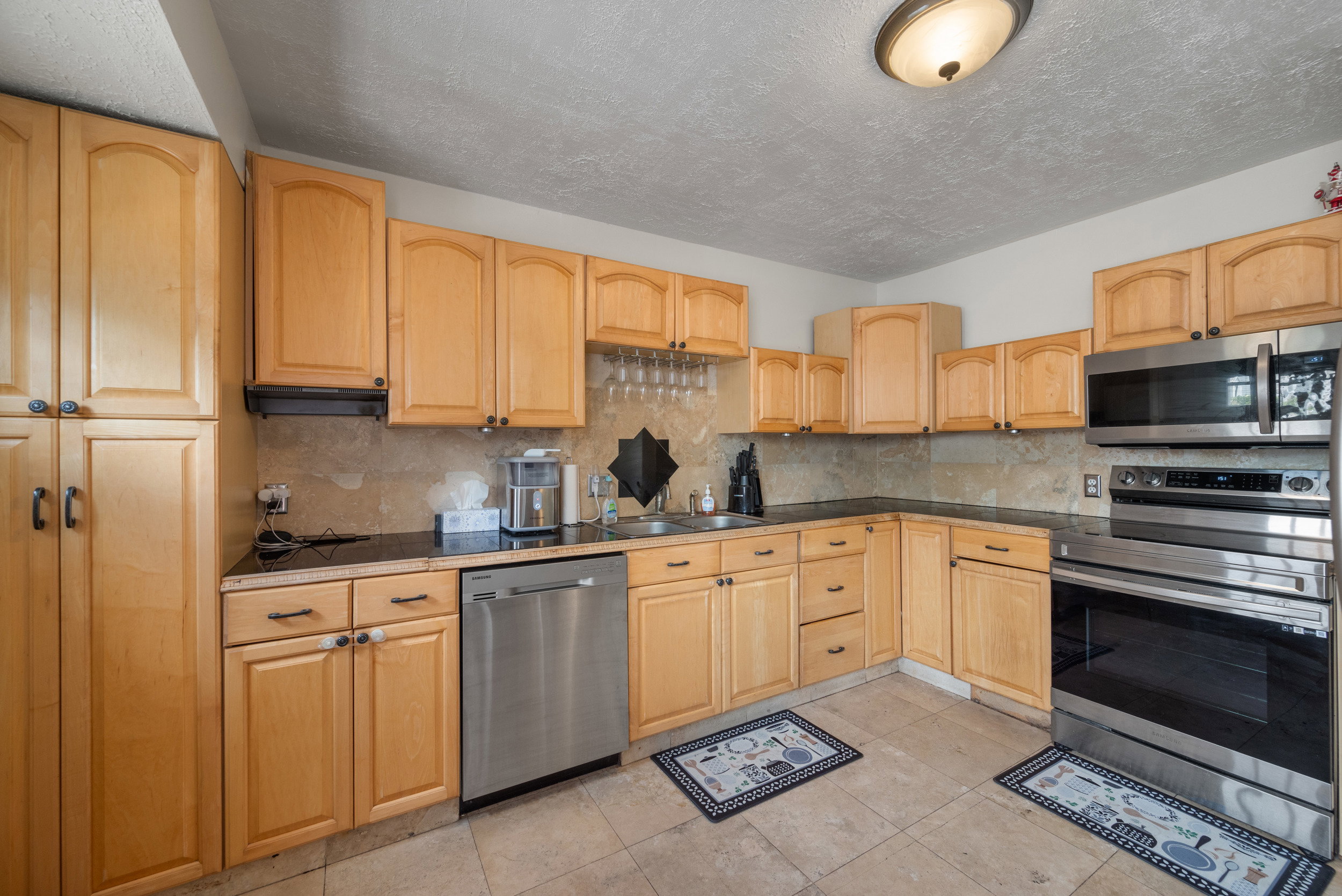 Kitchen featuring light wood cabinetry, stone-look tile flooring, and dark countertops