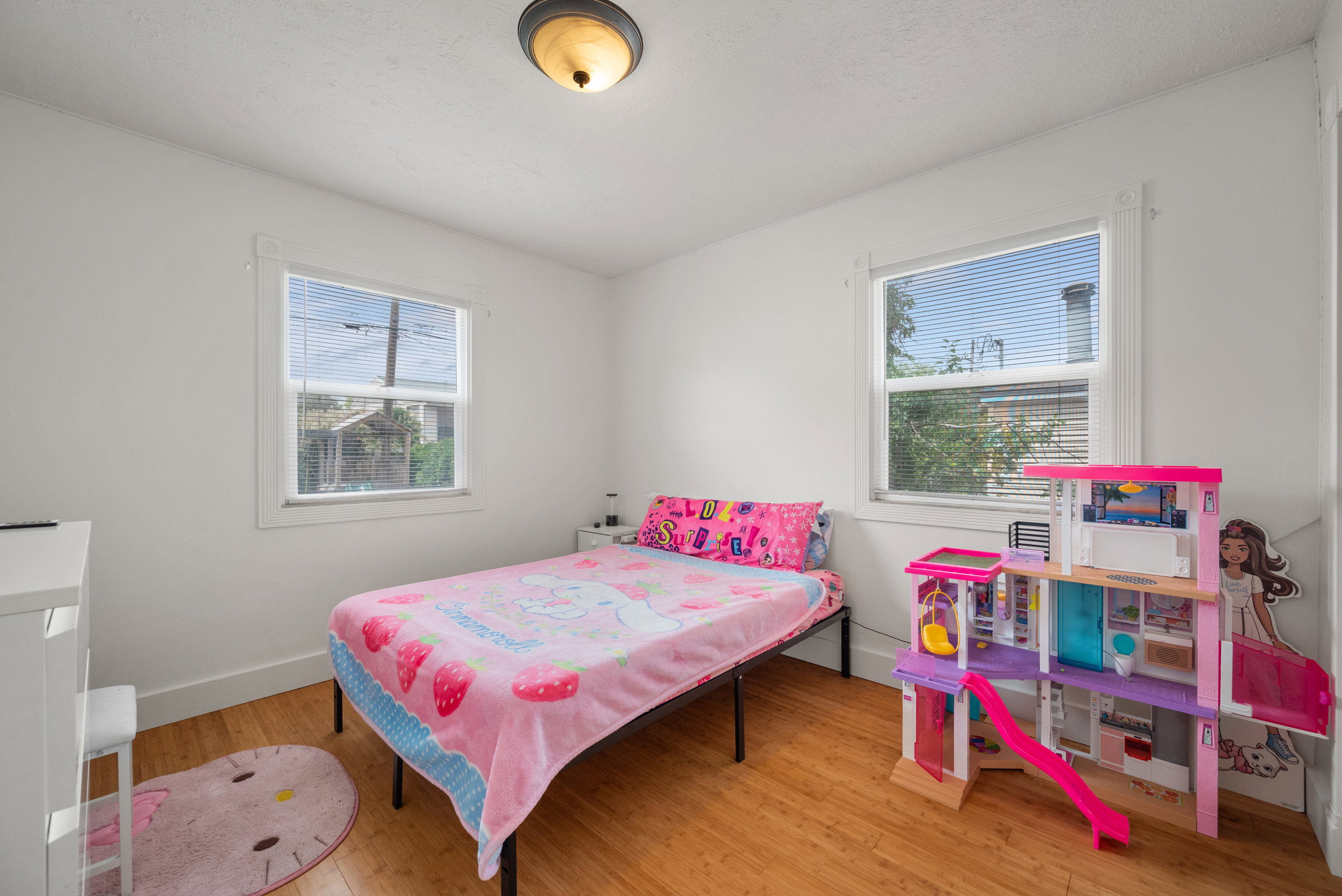 Bedroom featuring wood-finish flooring, two large windows, a ceiling-mounted light fixture, and white wall finishes