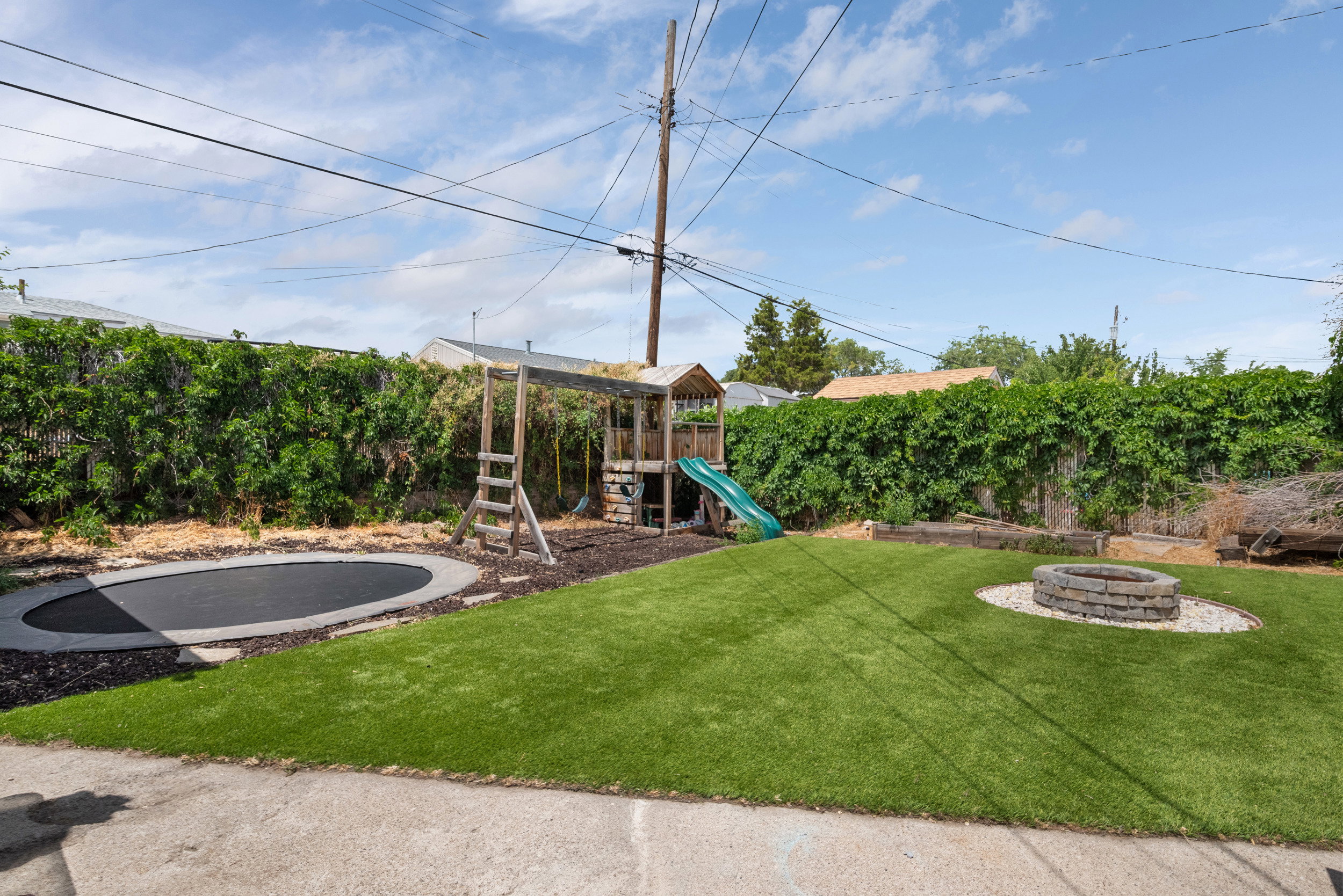 Expansive backyard featuring artificial turf, an in-ground trampoline, and a stone-ringed fire pit