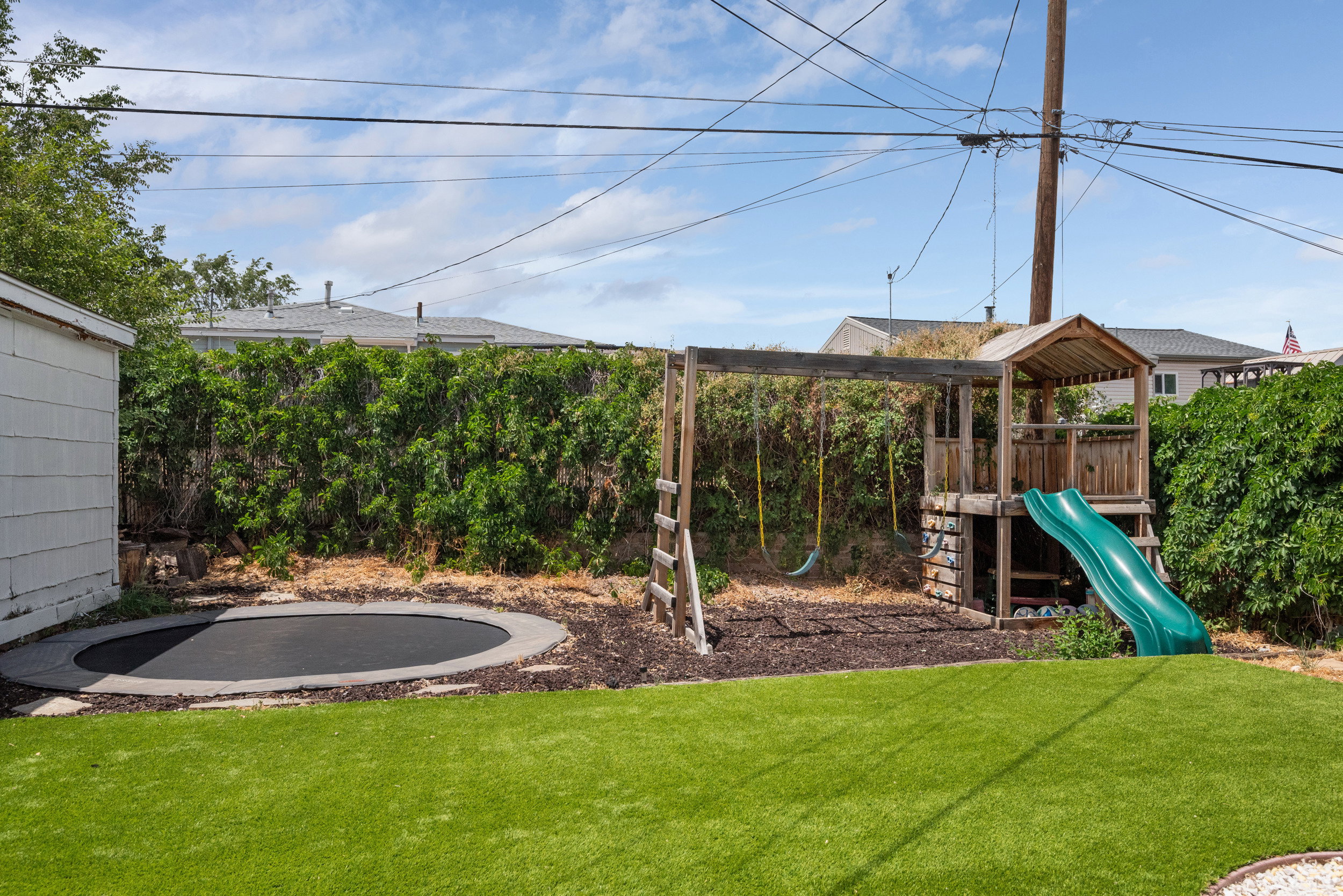 Backyard featuring artificial turf, built-in trampoline, and a wooden play structure with a slide and swings