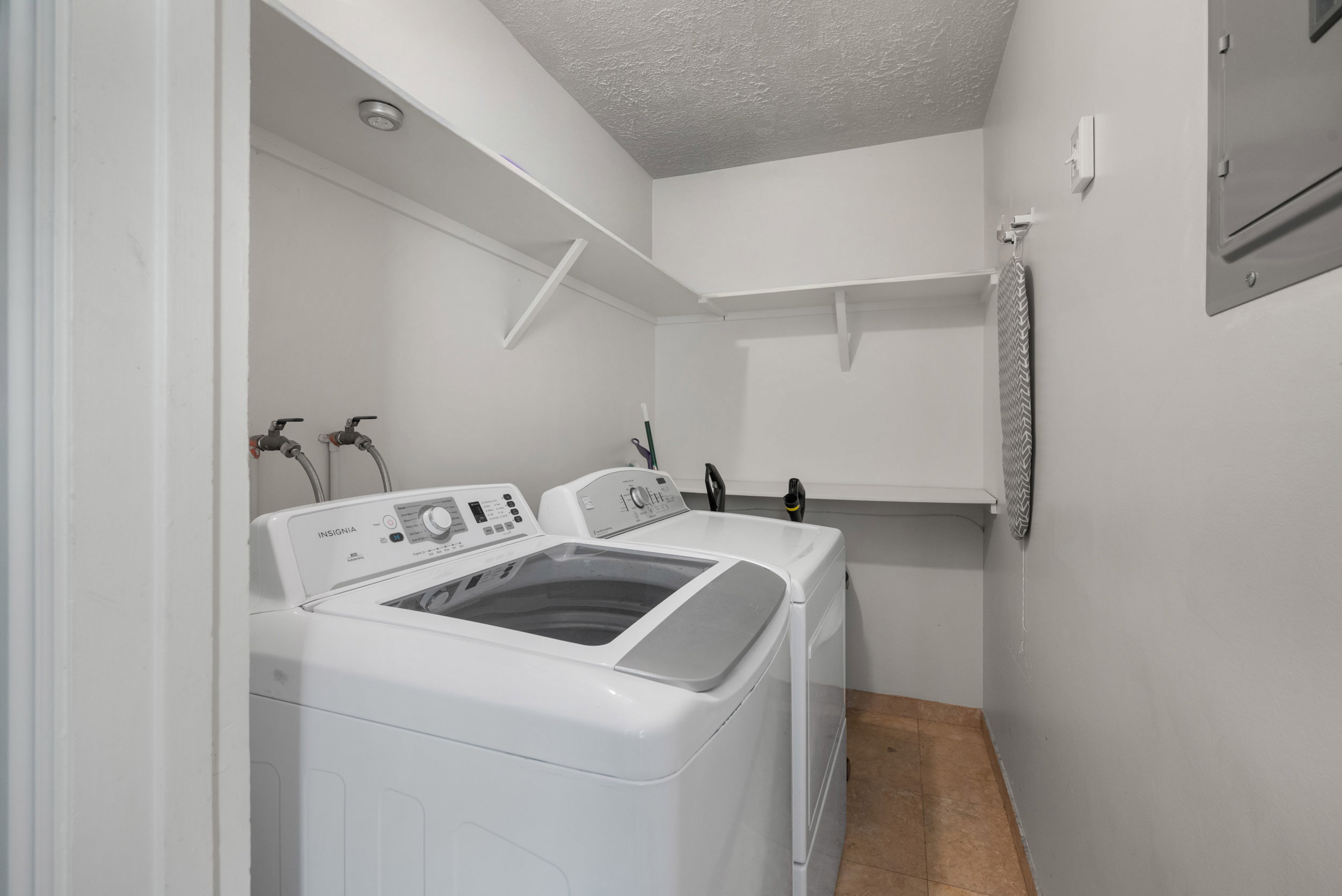 Dedicated laundry area featuring a top-load washing machine, a front-load dryer, and two wall-mounted storage shelves