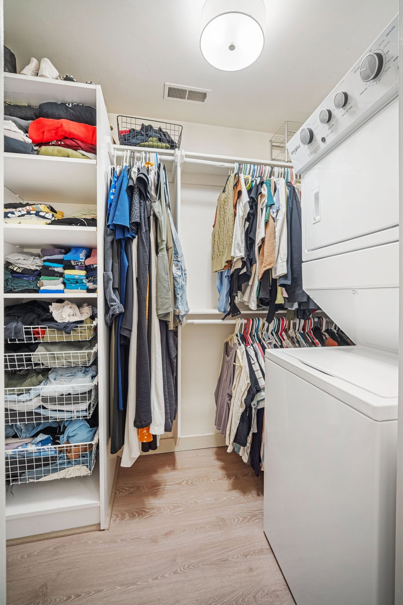 Laundry closet featuring a stacked washer and dryer, wood-finish flooring, built-in shelving, and hanging rod storage