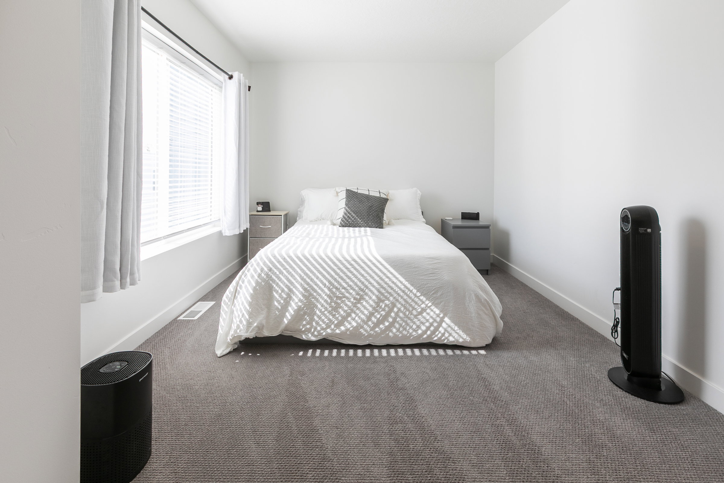 Bedroom featuring neutral-toned carpet, white walls, and a large window with blinds