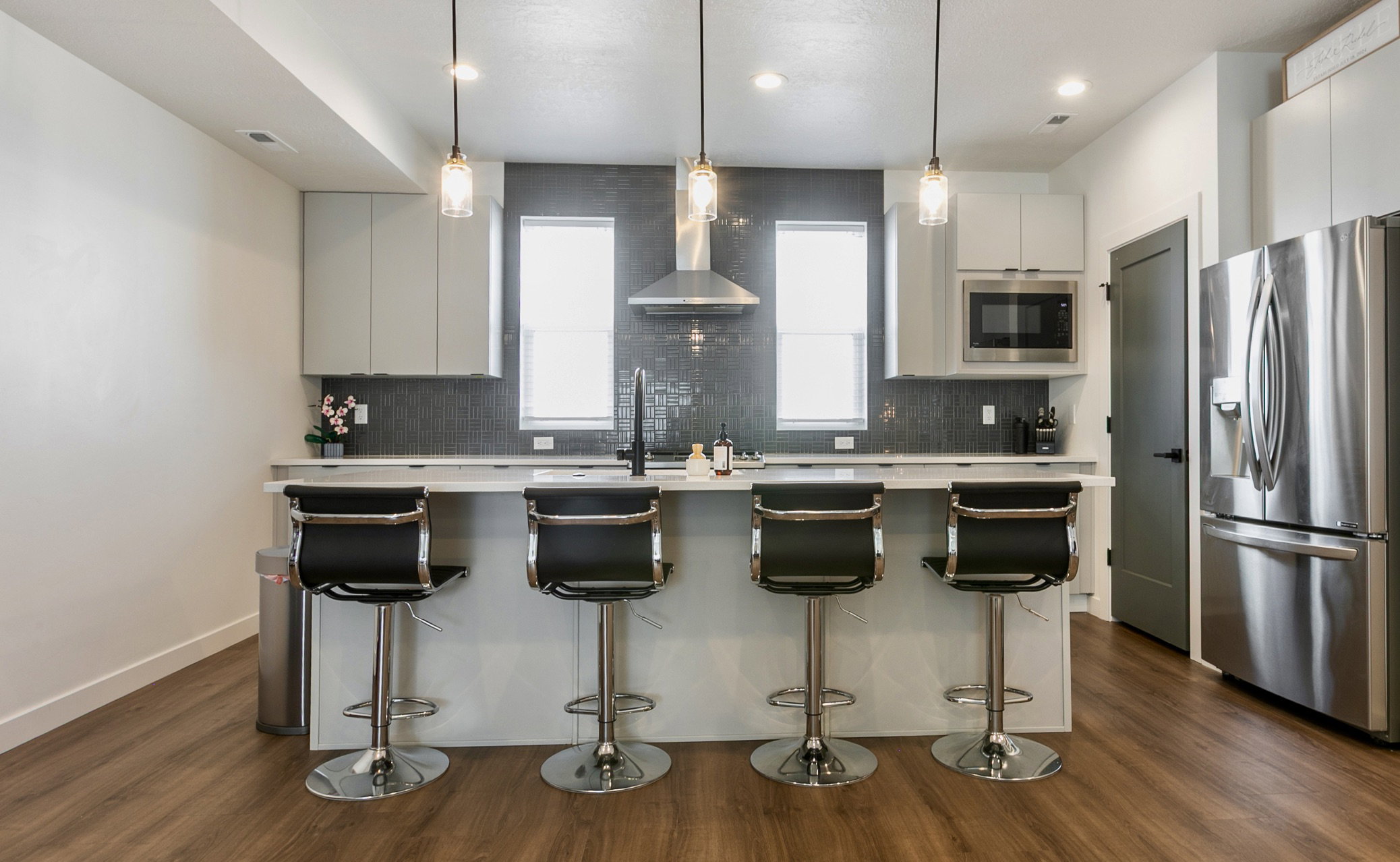 Contemporary kitchen featuring a large island with quartz countertop, stainless steel appliances, upper cabinetry, and wood-finish flooring