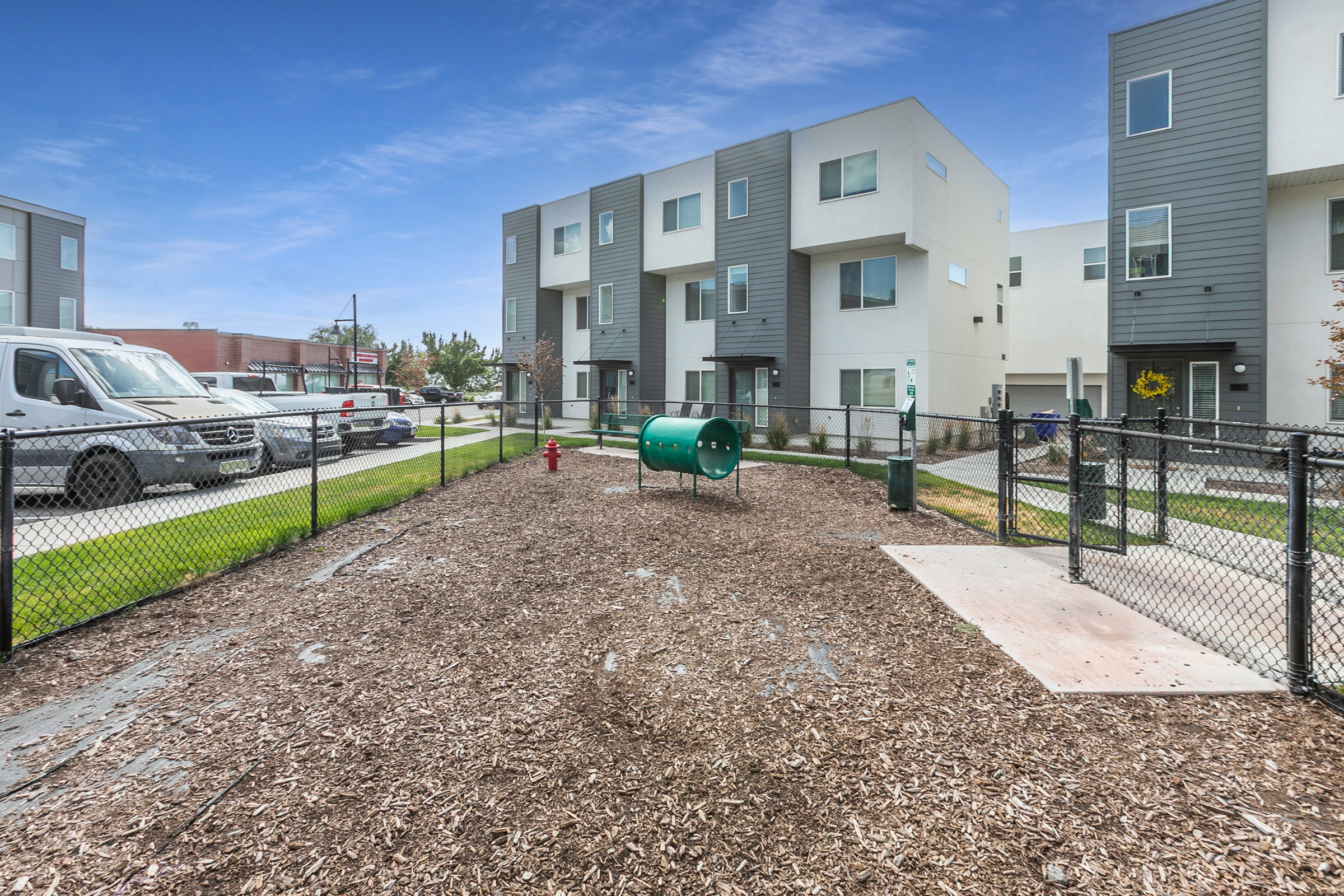 Fenced outdoor area featuring wood chip ground cover, a green play tunnel, and a red fire hydrant