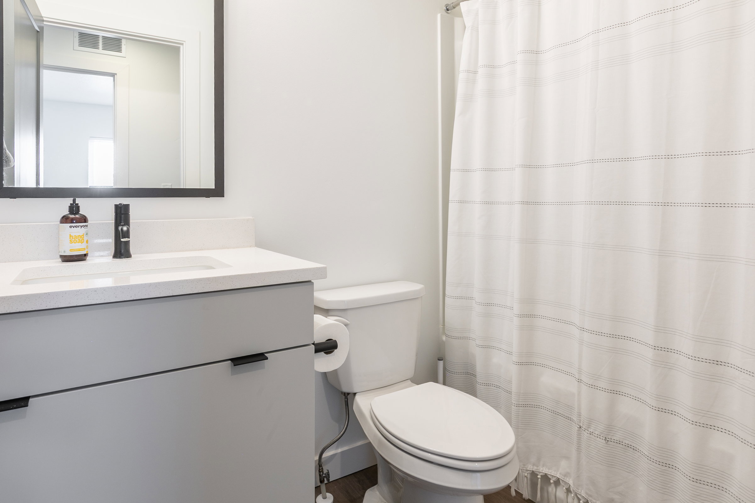 Bathroom featuring a white integrated sink, light gray vanity with black hardware, black framed mirror, and a white toilet