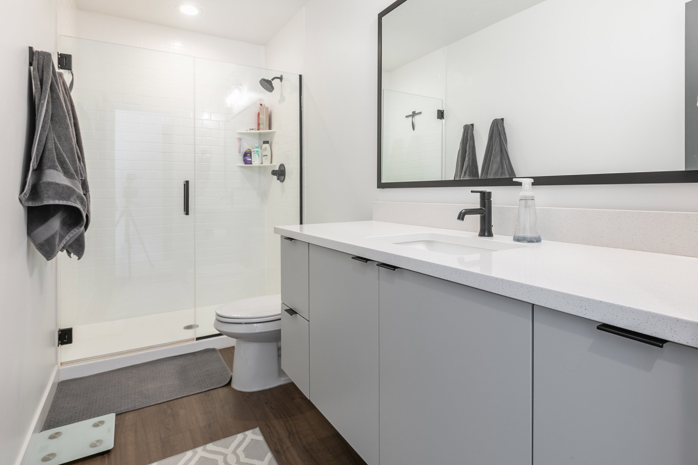 Contemporary bathroom featuring a spacious glass-enclosed shower with white subway tile, a wide vanity with light gray cabinetry, a white countertop, and a large framed mirror