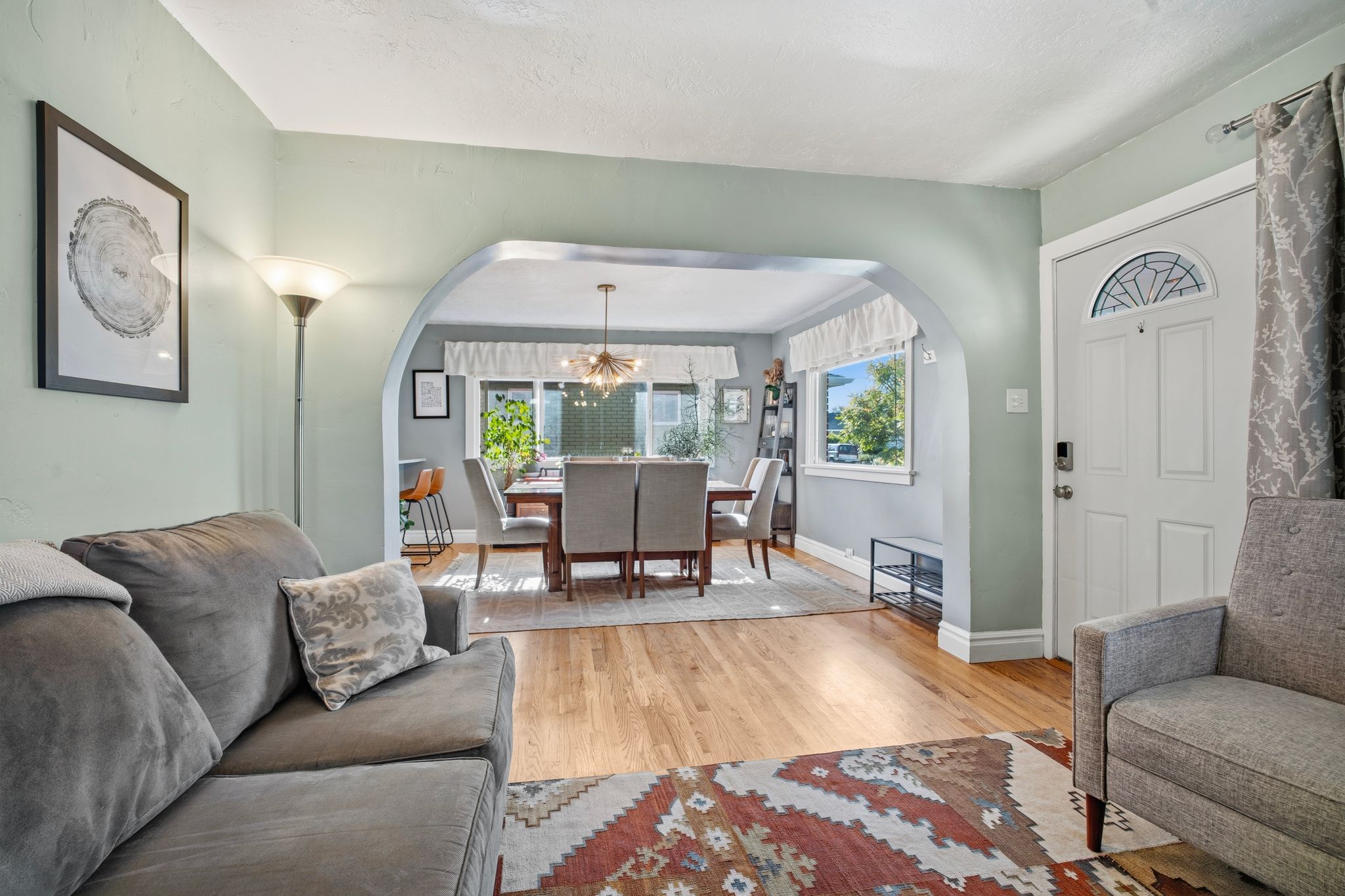 Archway entry to the dining area featuring wood-finish flooring, light green wall paint, and a white front door with a decorative glass insert