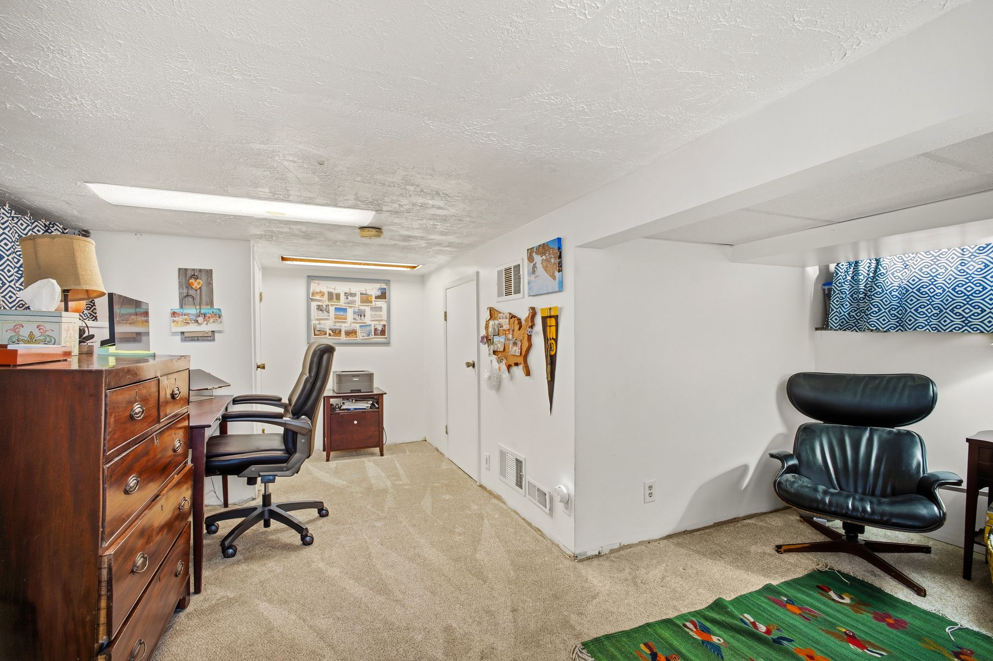 Carpeted room with white walls, featuring a window with patterned curtains, a built-in beam, and multiple doors