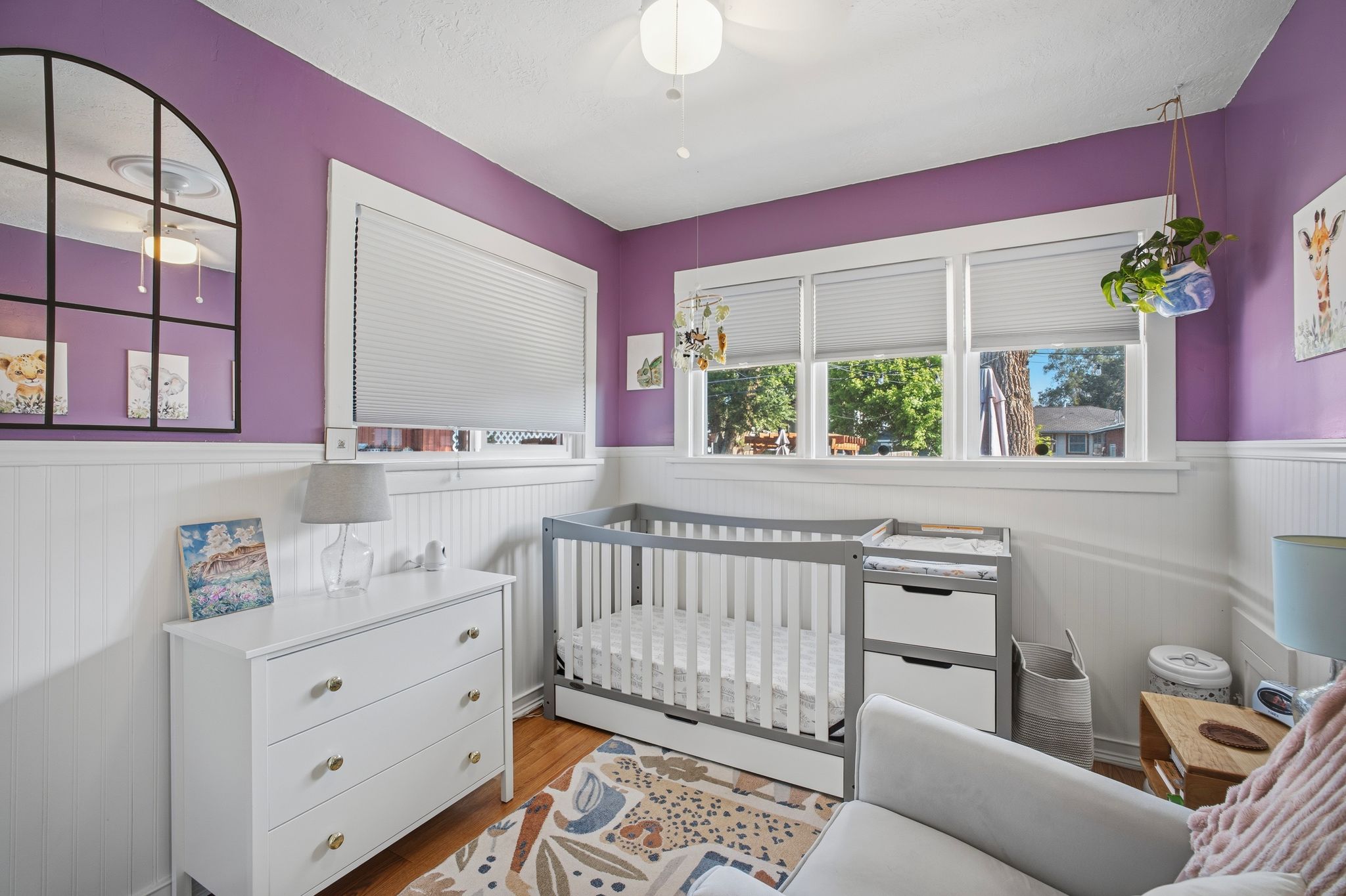 Room featuring wood-finish flooring, white beadboard wainscoting, and a multi-pane window with white cellular blinds