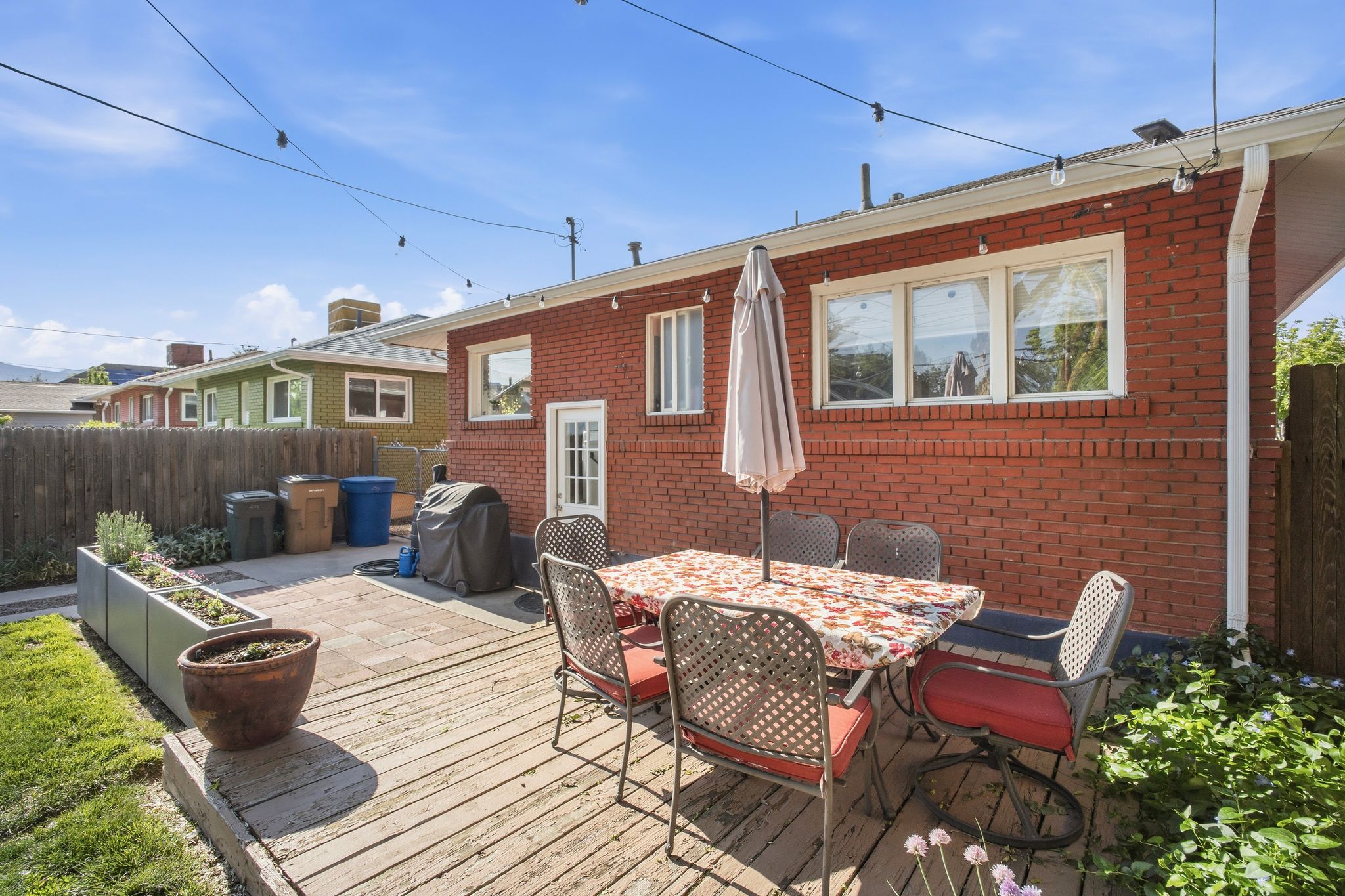 Expansive outdoor living area featuring a wood deck, paver patio, brick exterior, and multiple windows