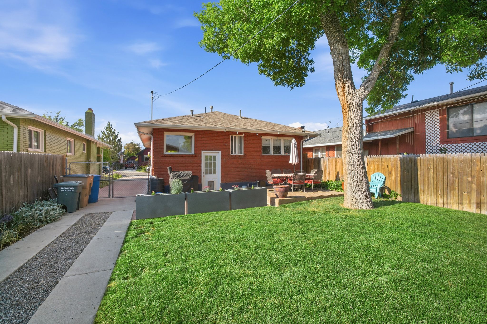 Expansive backyard featuring a lush lawn, mature shade tree, and a concrete patio