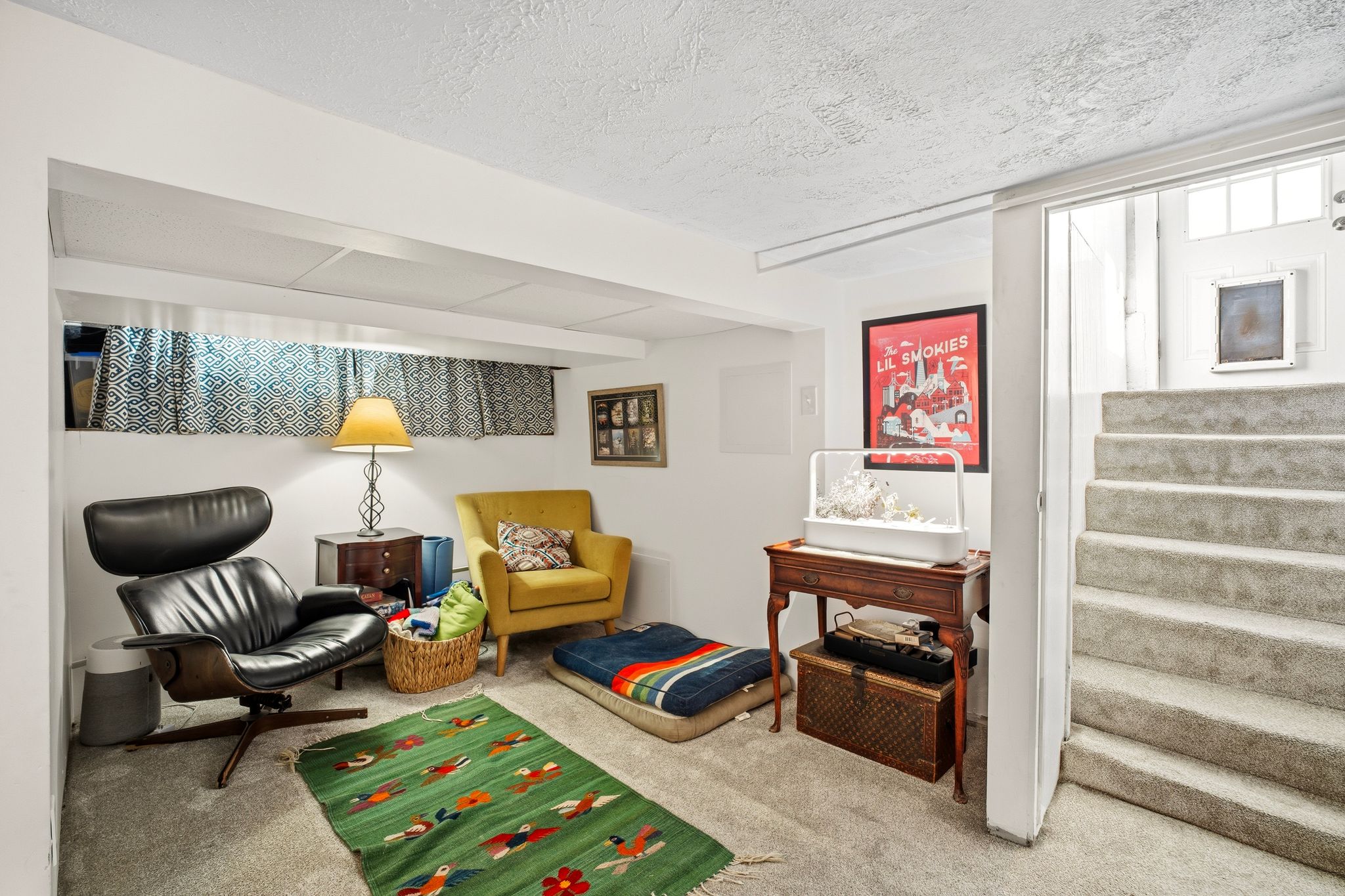 Carpeted stairs leading to a lower-level room with a horizontal window and exposed ceiling beams