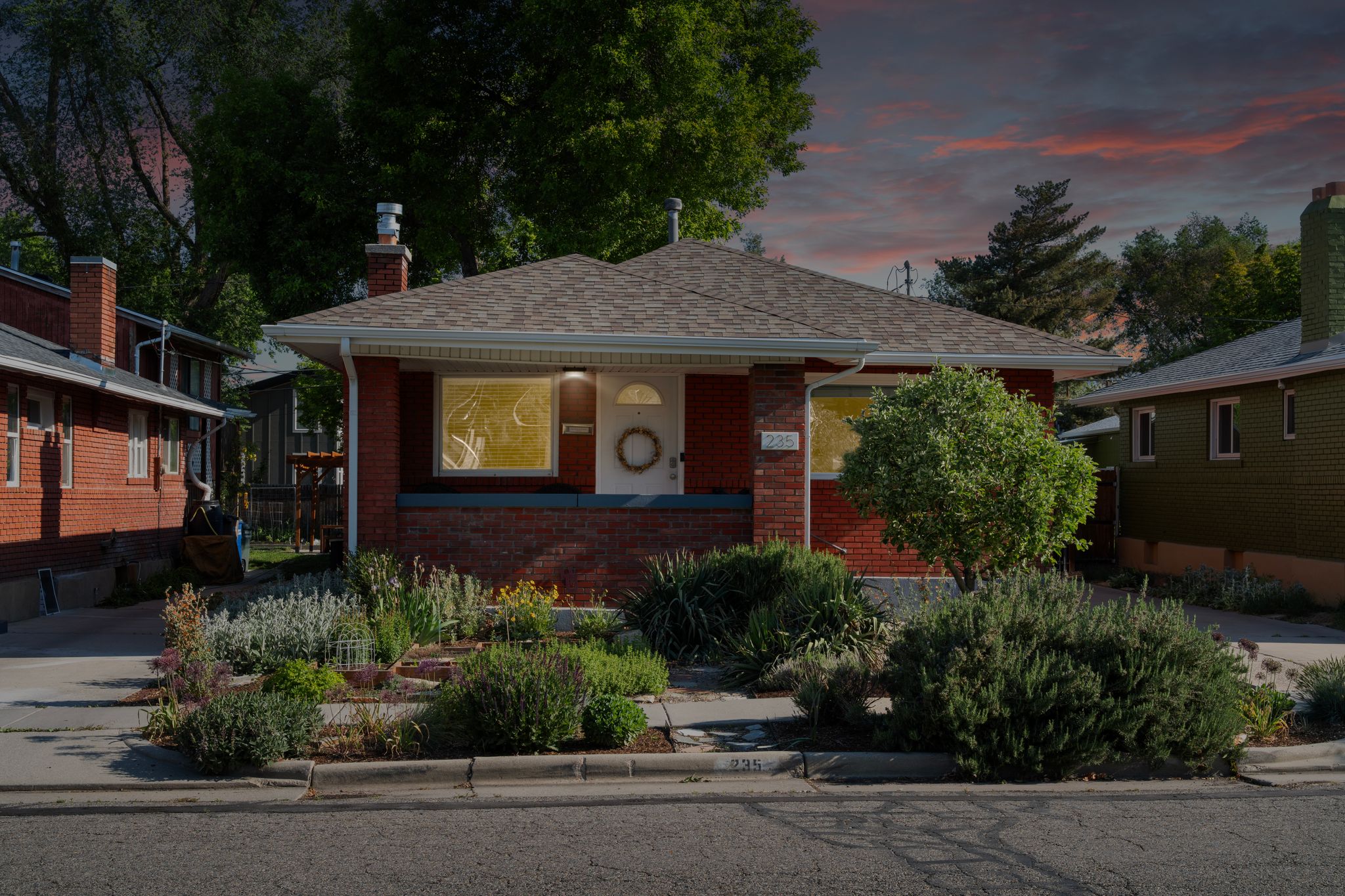 Brick facade residence featuring a front porch, a well-maintained shingle roof, and a mature front yard landscaping