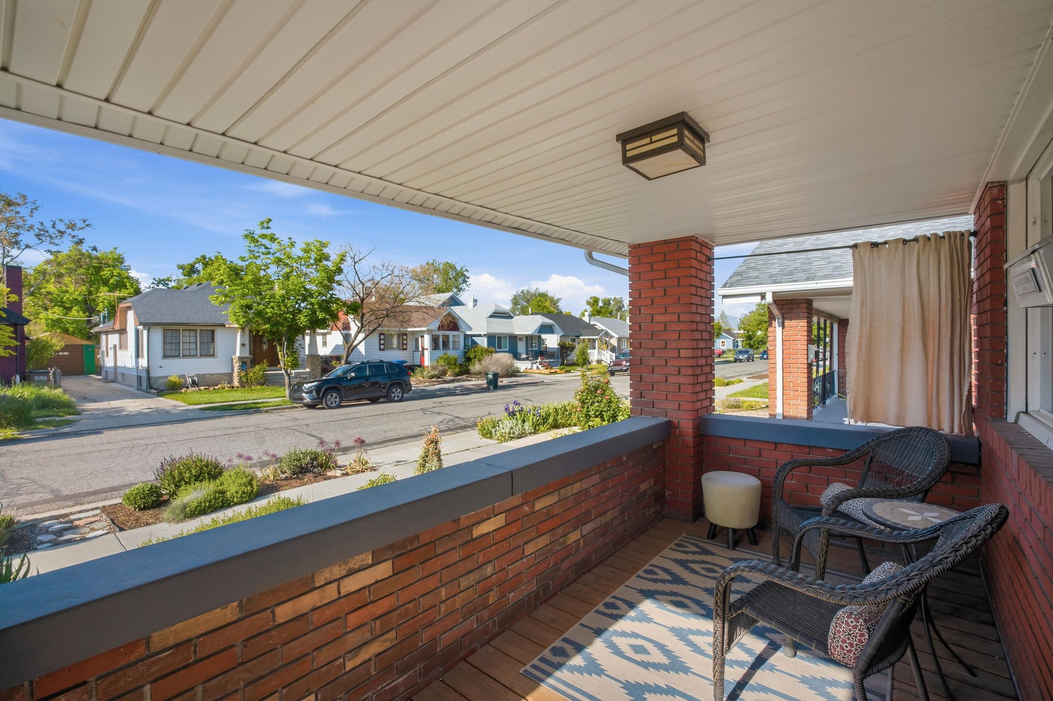 Inviting front porch featuring a brick half-wall, brick support columns, white soffit ceiling, and a flush-mount ceiling light fixture