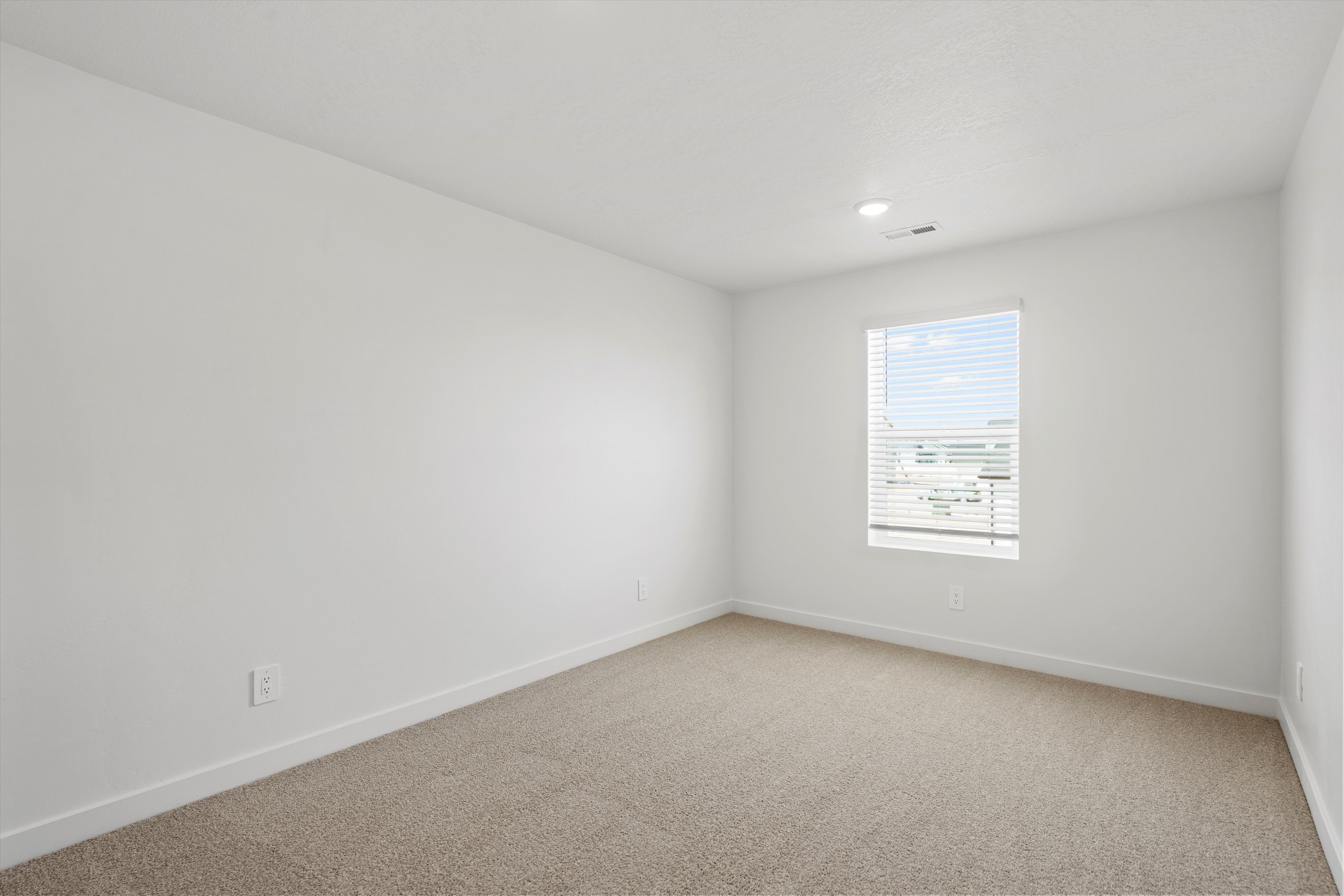 Spacious room featuring neutral carpet flooring, white walls, and a single window with blinds