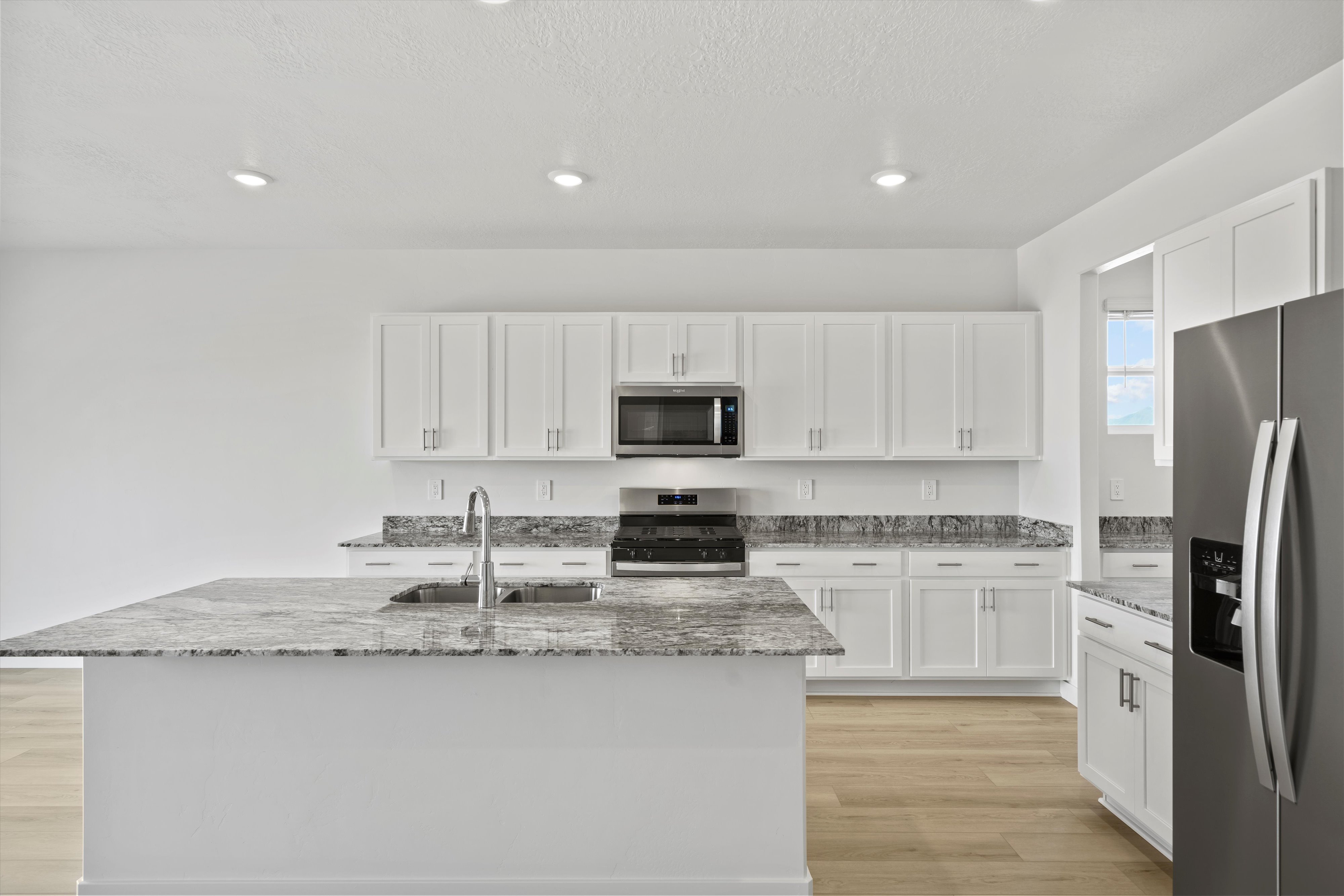 Kitchen featuring a large island with sink, white shaker cabinetry, stainless steel appliances, granite countertops, and light wood-finish flooring