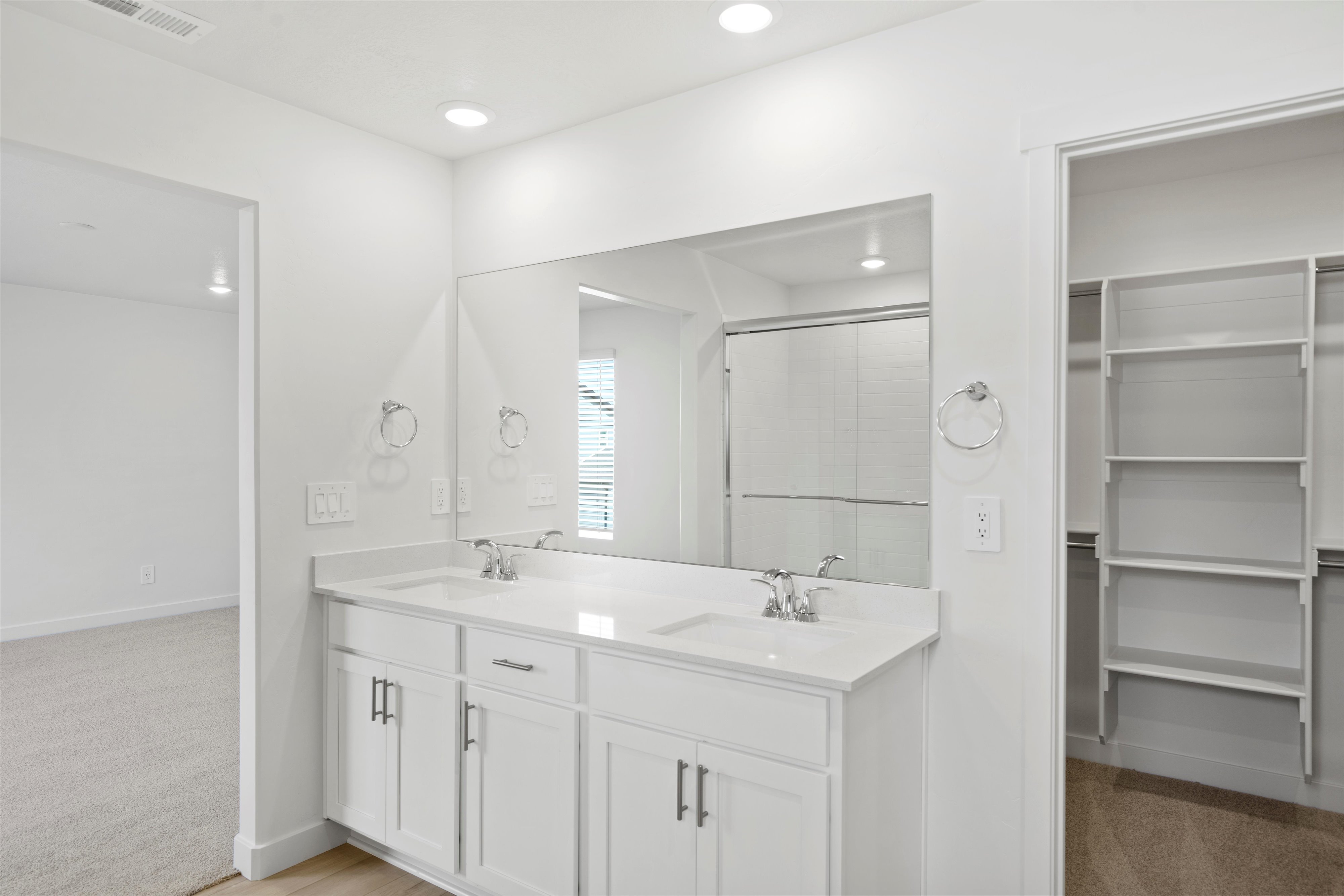 Dual vanity with white shaker-style cabinetry, chrome fixtures, and a large wall-mounted mirror