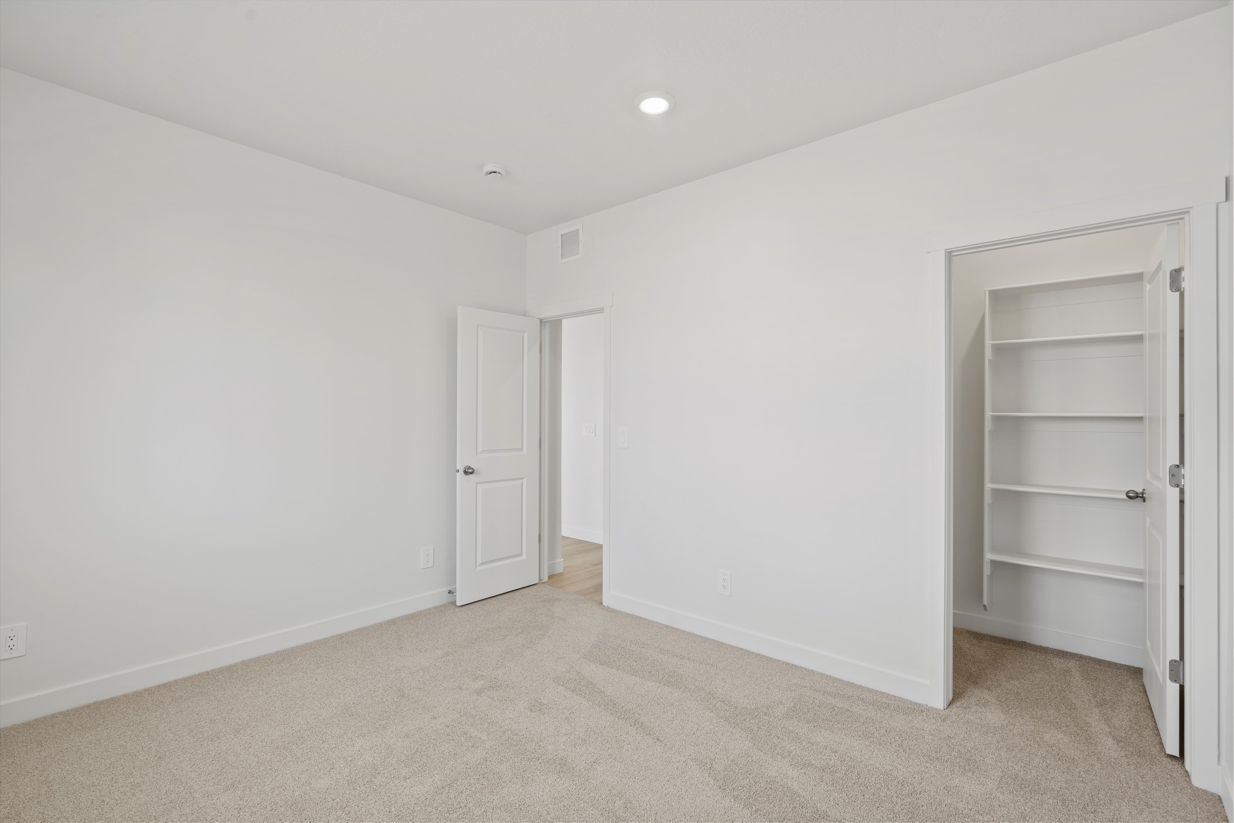 Neutral-toned room featuring a soft carpet, white walls, and a recessed ceiling light