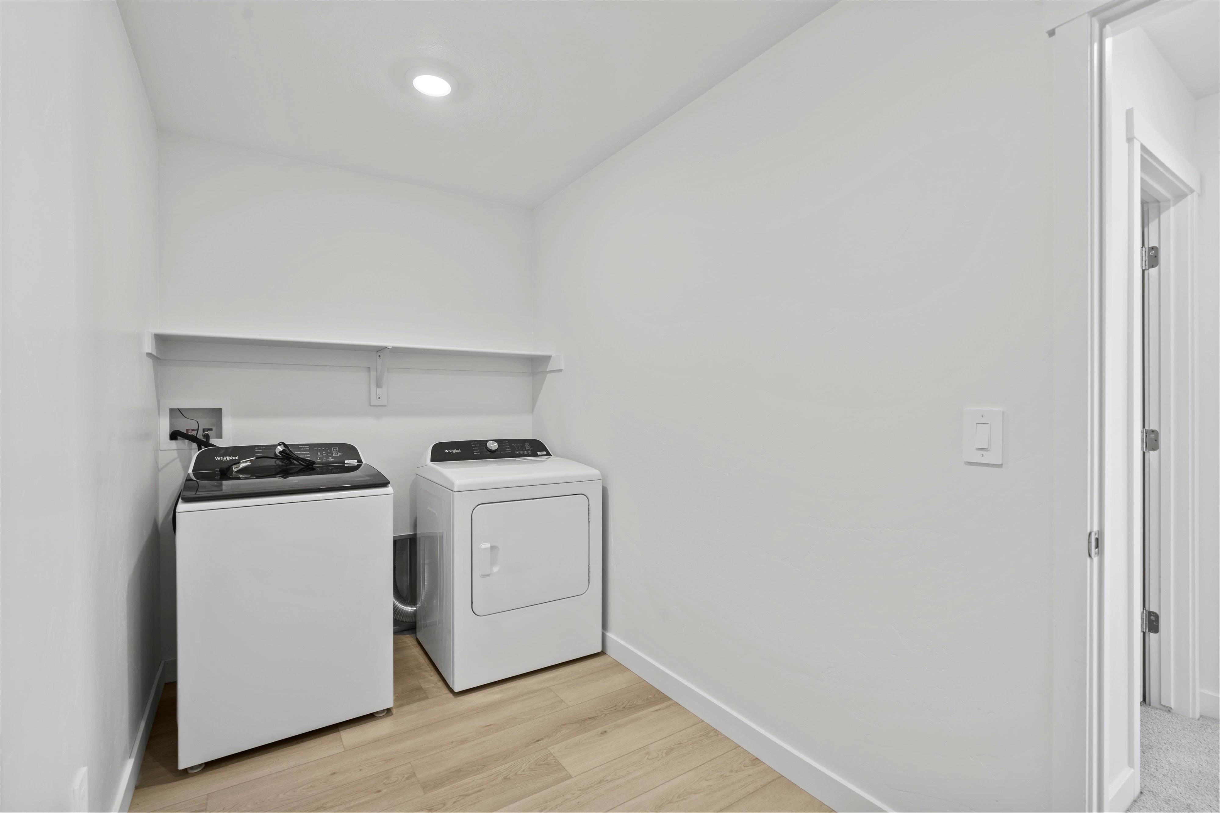 Dedicated laundry area featuring wood-finish flooring, white walls, and an overhead shelf