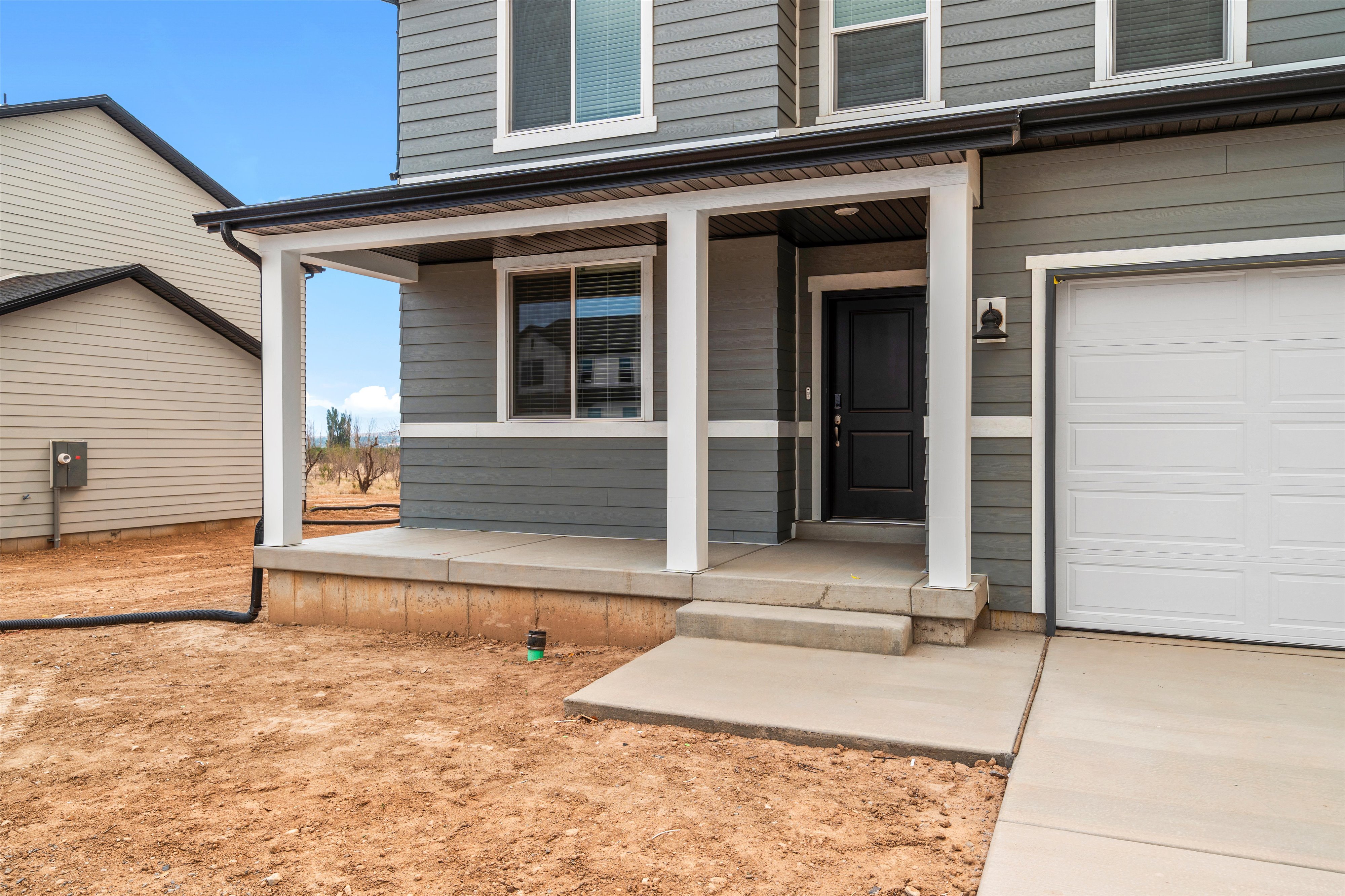 Contemporary exterior featuring gray siding, a white garage door, and a covered entryway with a black front door