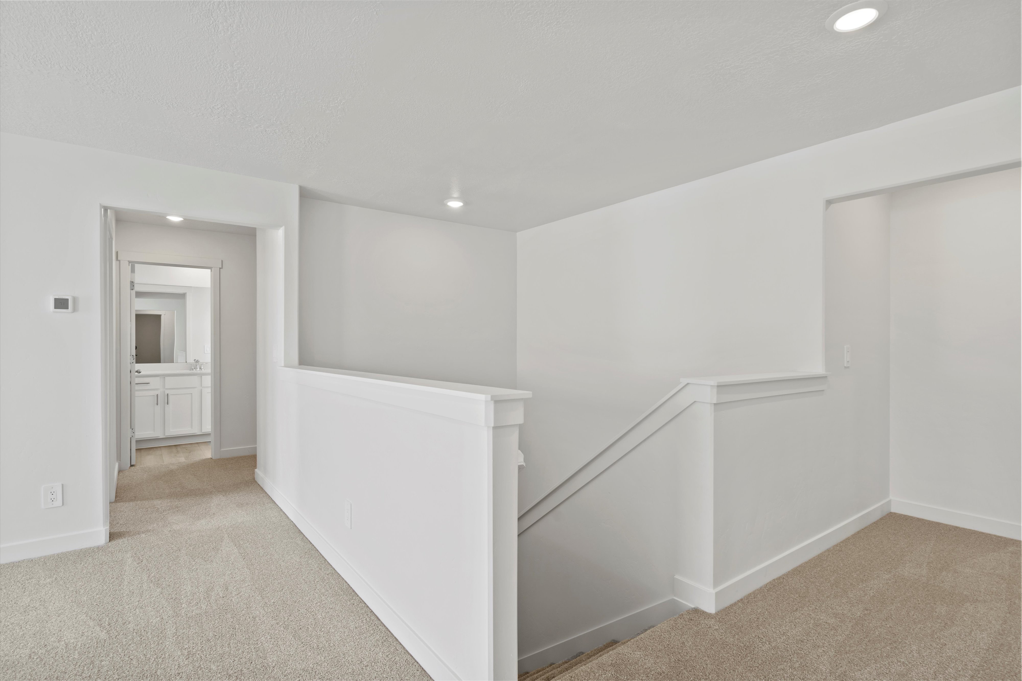 Upper-level landing featuring neutral carpeting, white trim, recessed lighting, and a partial view of a bathroom vanity