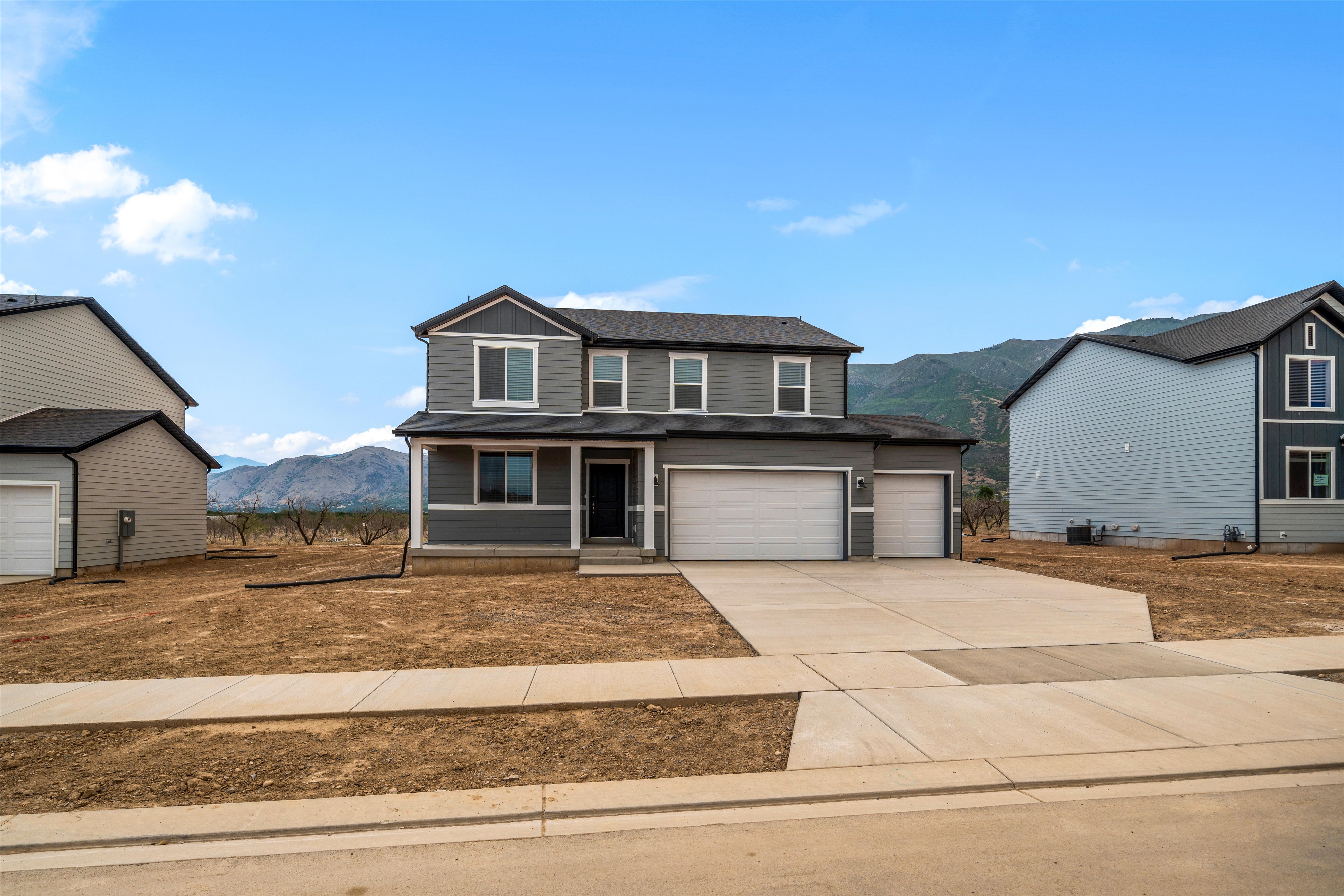 Two-story home featuring a charcoal gray facade with white trim, a covered front porch, and a two-car garage with an additional single-car garage