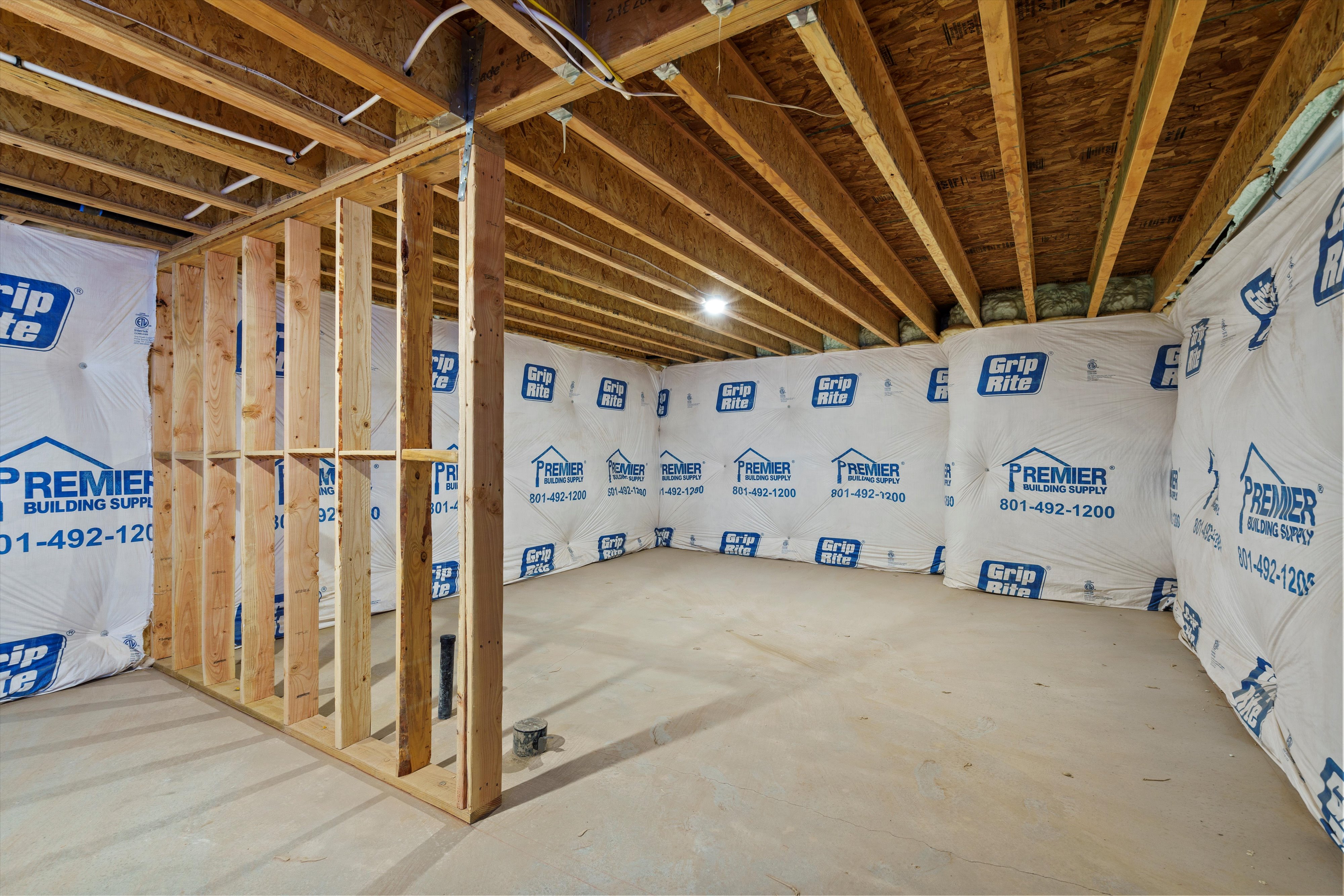 Unfinished basement featuring exposed wood joists and subfloor, partial wood framing for interior walls, concrete flooring, and wrapped exterior foundation walls