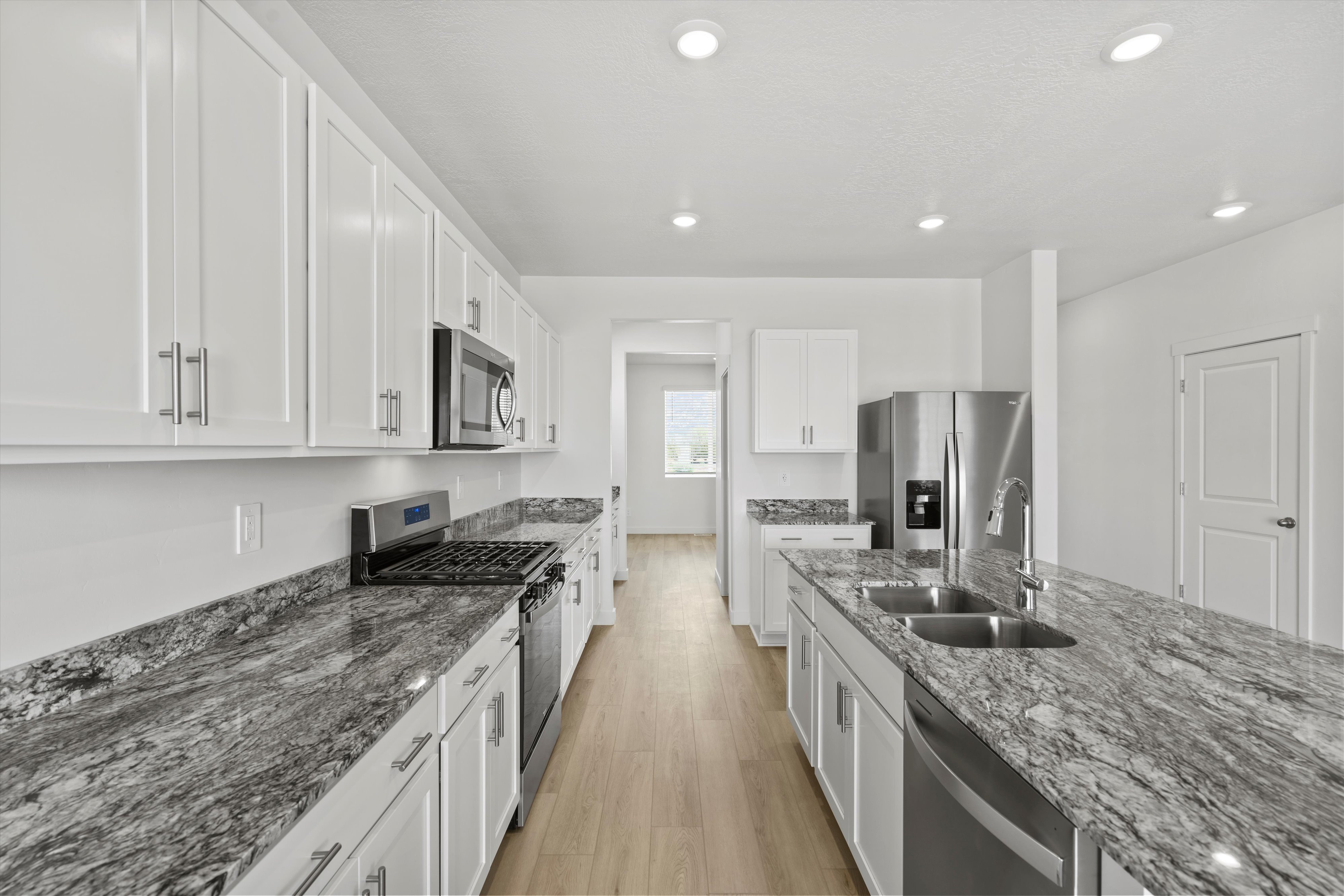 Contemporary kitchen with extensive white cabinetry, stainless steel appliances, striking patterned stone countertops, and wood-finish flooring