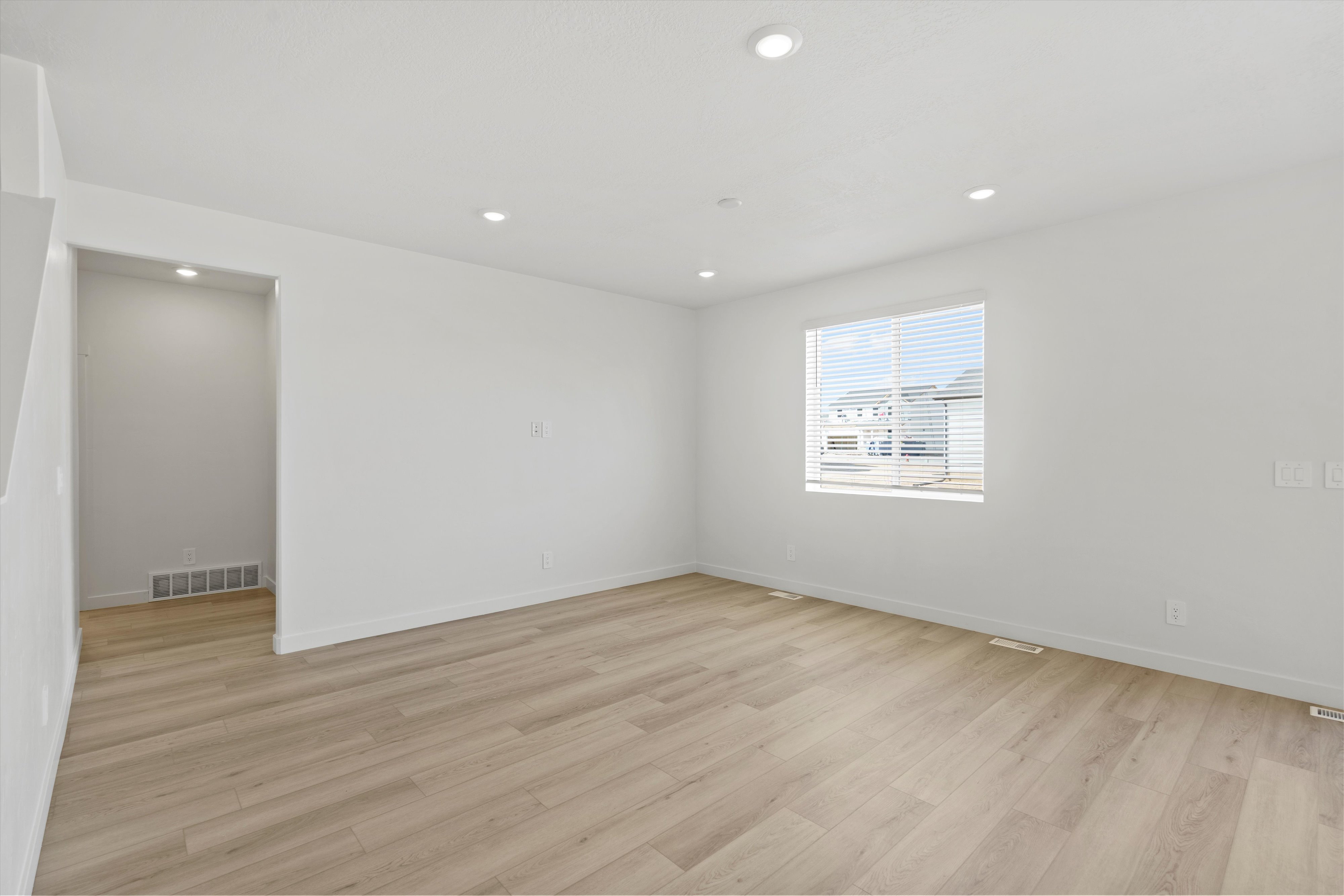 Bright interior space featuring wood-finish flooring, recessed lighting, white walls, a large window with blinds, and white baseboards