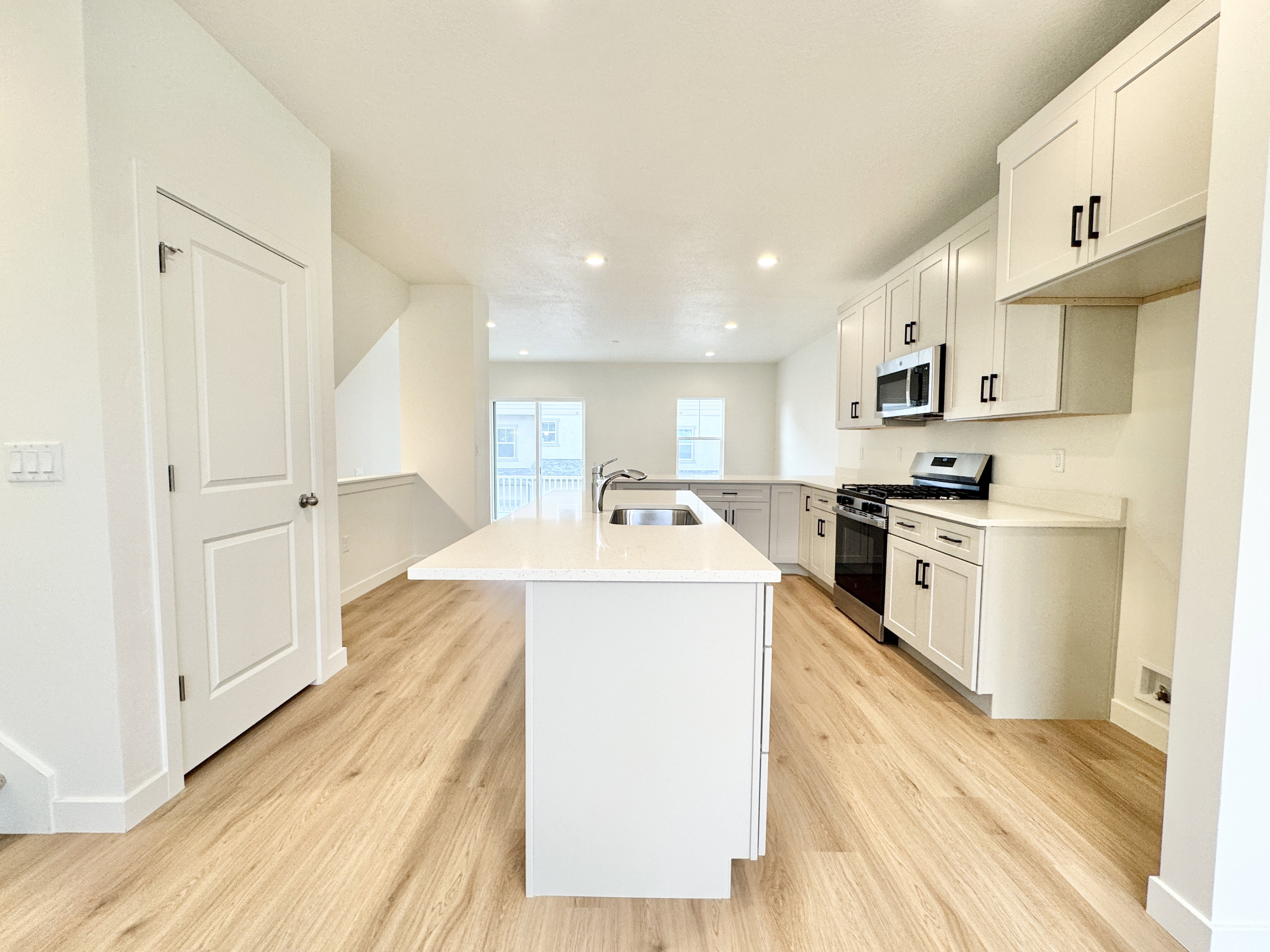 Modern kitchen featuring a central island with an undermount sink, white cabinetry with dark hardware, stainless steel appliances, and wood-finish flooring