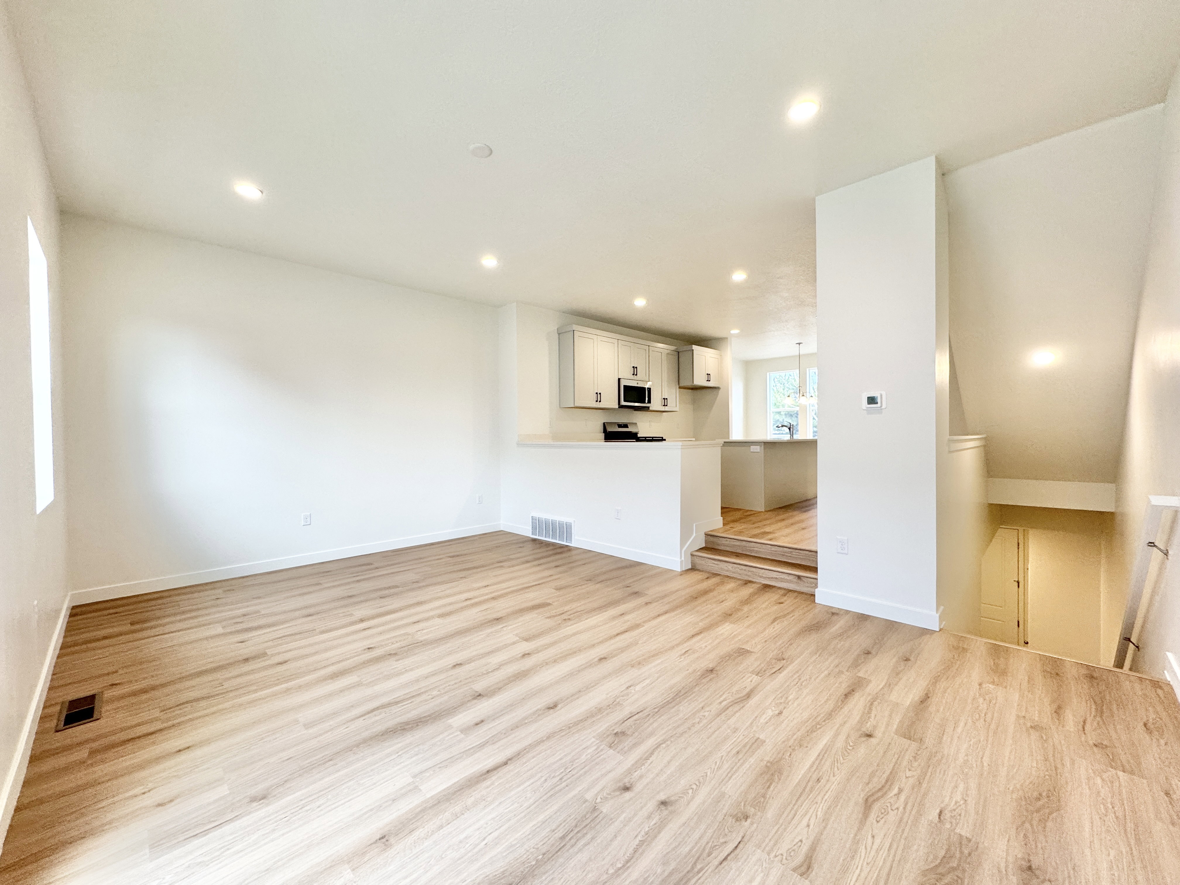 Open-concept living space featuring light wood-finish flooring, recessed ceiling lighting, and a kitchen with light cabinetry and built-in microwave