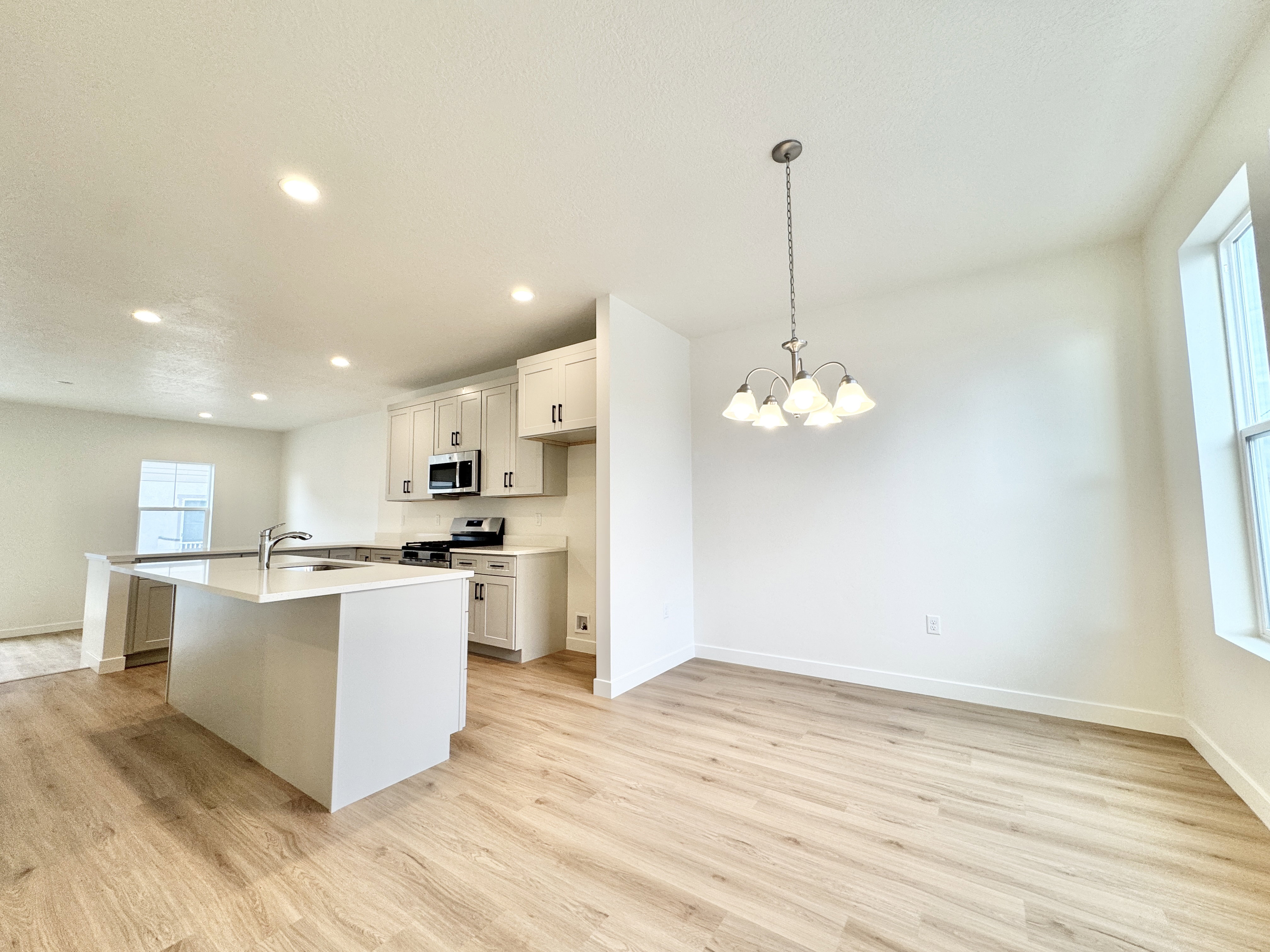 Open-concept living space featuring wood-finish flooring, a contemporary kitchen island with a built-in sink, stainless steel appliances, light-toned cabinetry, and recessed lighting