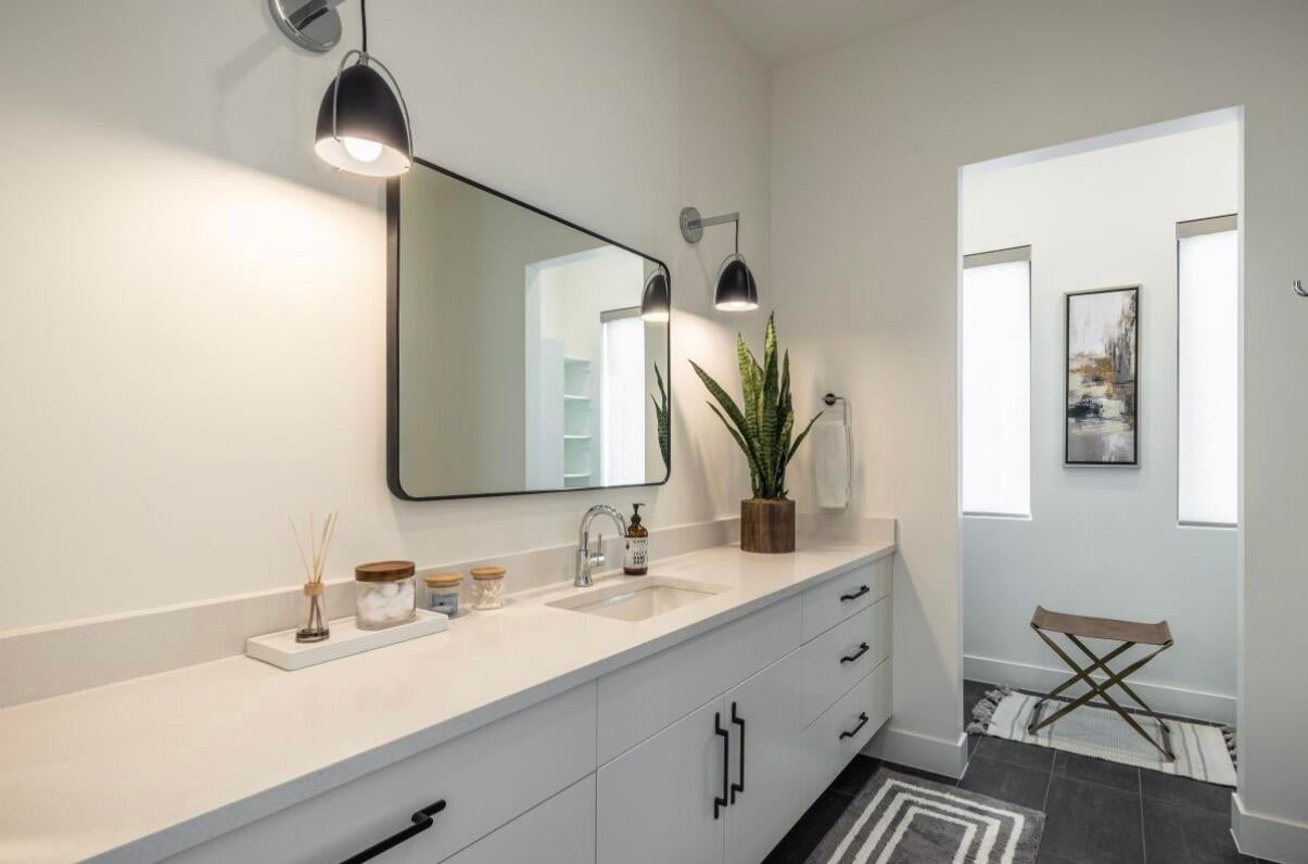 Bathroom featuring a dual-sink vanity with light-toned countertops, white cabinetry with black hardware, and integrated wall sconces