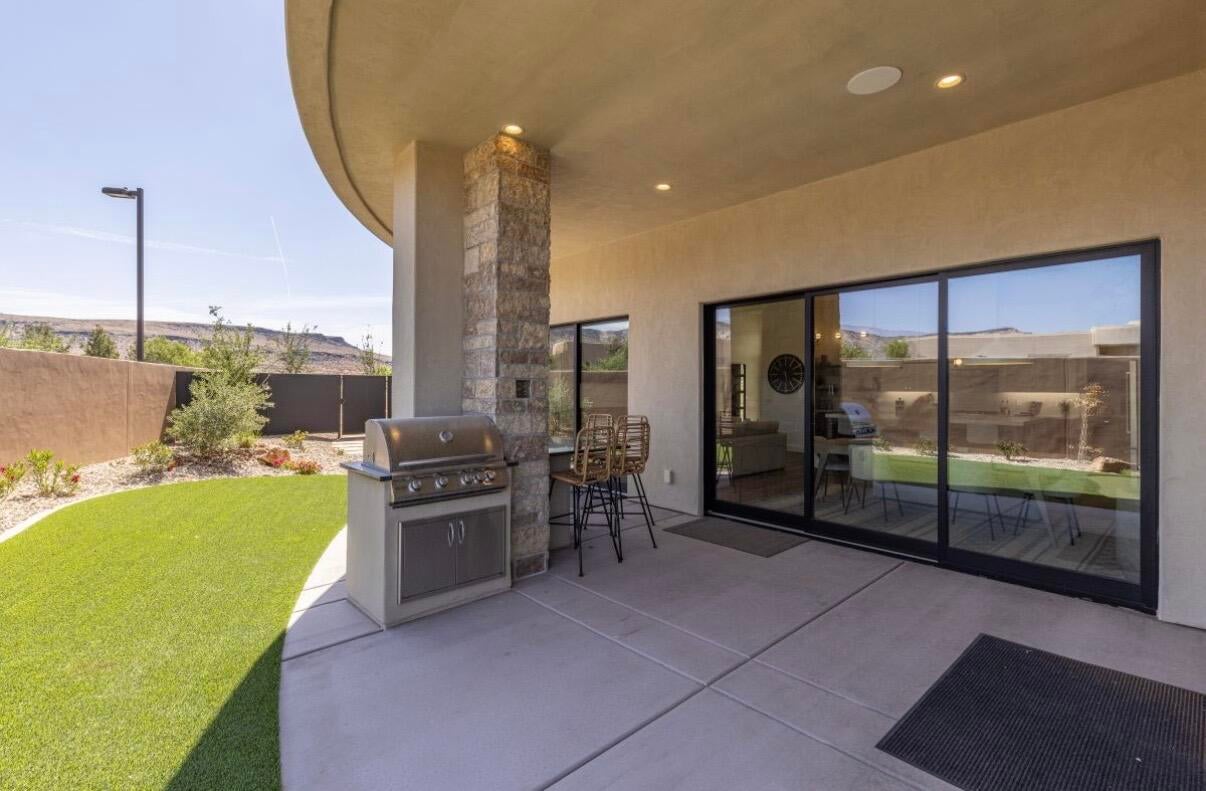 Expansive outdoor living area featuring a built-in grill, concrete patio, artificial turf, and a stone-clad column