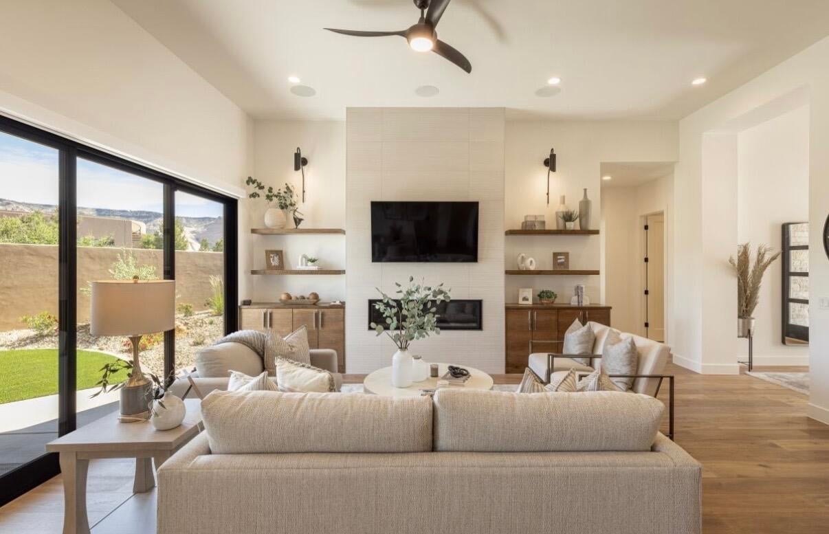 Spacious living area featuring a large fireplace with a tile surround, built-in shelving, wood-finish flooring, and a modern ceiling fan