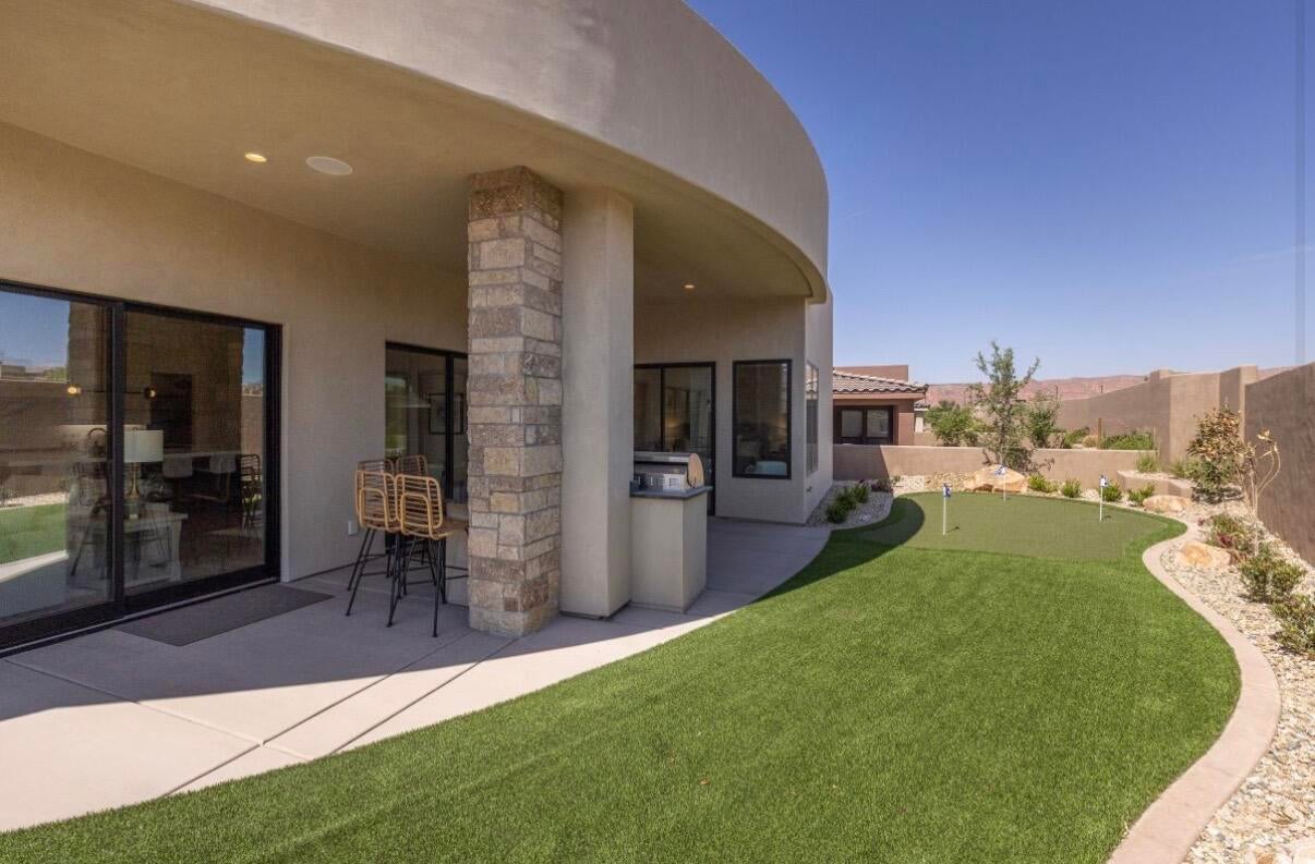 Covered patio with an outdoor kitchen, artificial turf lawn, putting green, and desert landscaping