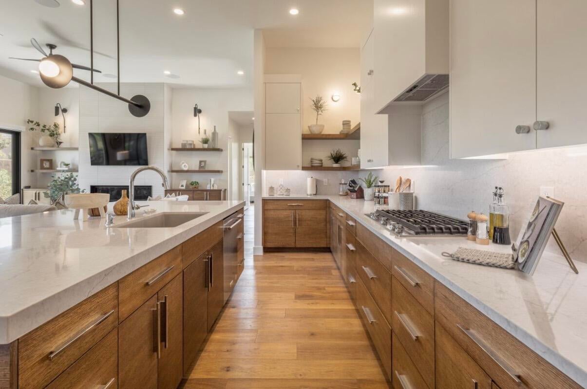 Modern kitchen featuring light wood-finish flooring, an expansive island with an undermount sink, a gas cooktop, and a built-in range hood