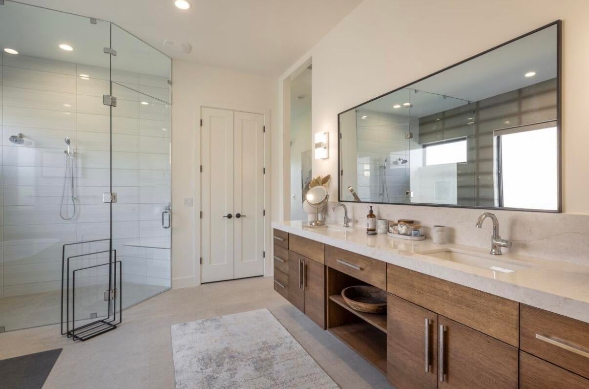 Contemporary bathroom featuring a dual vanity with wood-finish cabinetry and integrated sinks, a large frameless mirror, and a spacious glass-enclosed shower with subway tile surround and a built-in bench