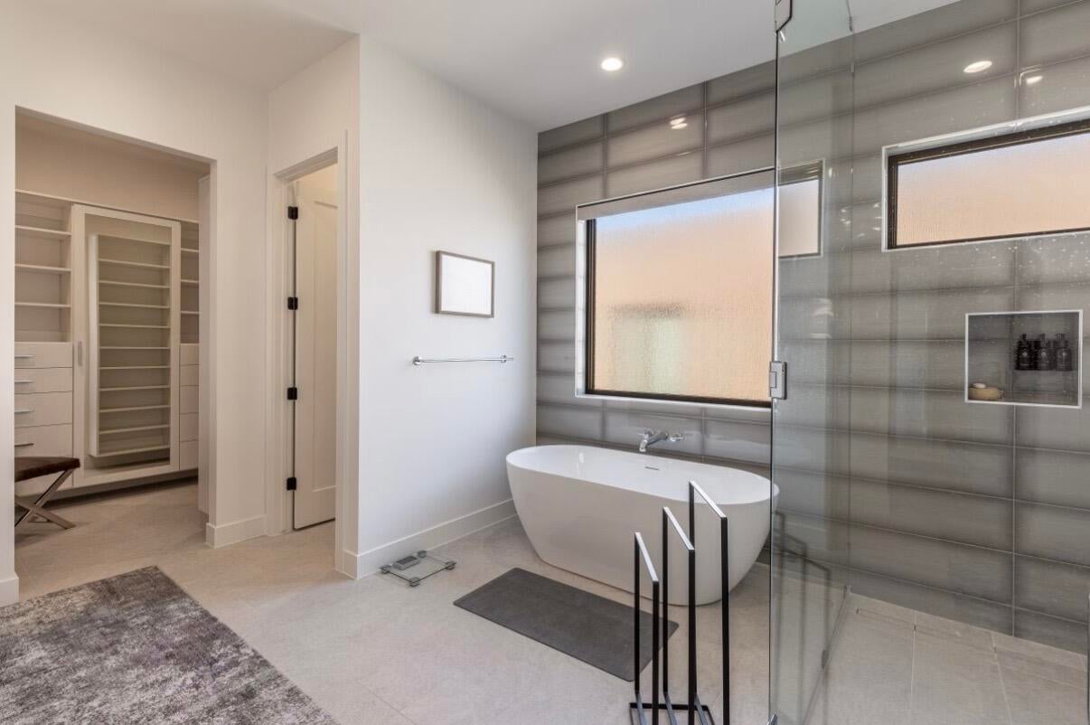 Freestanding soaking tub with a wall-mounted faucet, framed by two frosted windows, set against a tiled accent wall