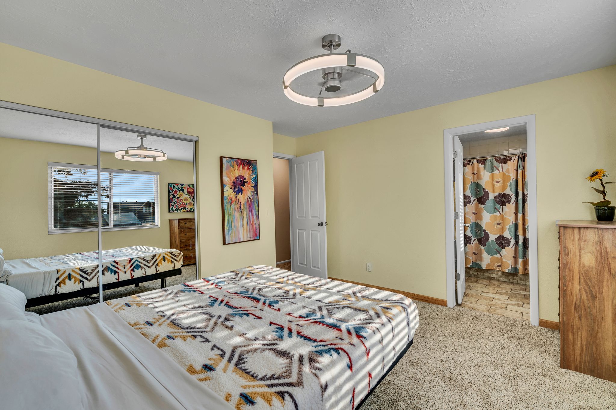 Carpeted room featuring a ceiling fan with integrated lighting, a window with blinds, and sliding mirrored closet doors